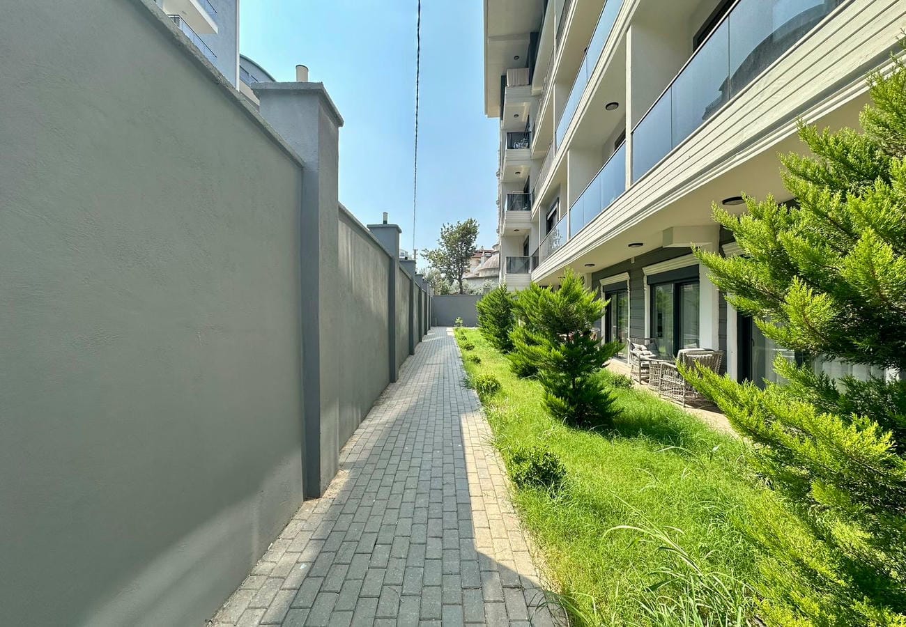 Alanya’da satıştaki binanın cephesi boyunca iğne yapraklı çalılarla gri taş döşeli yol