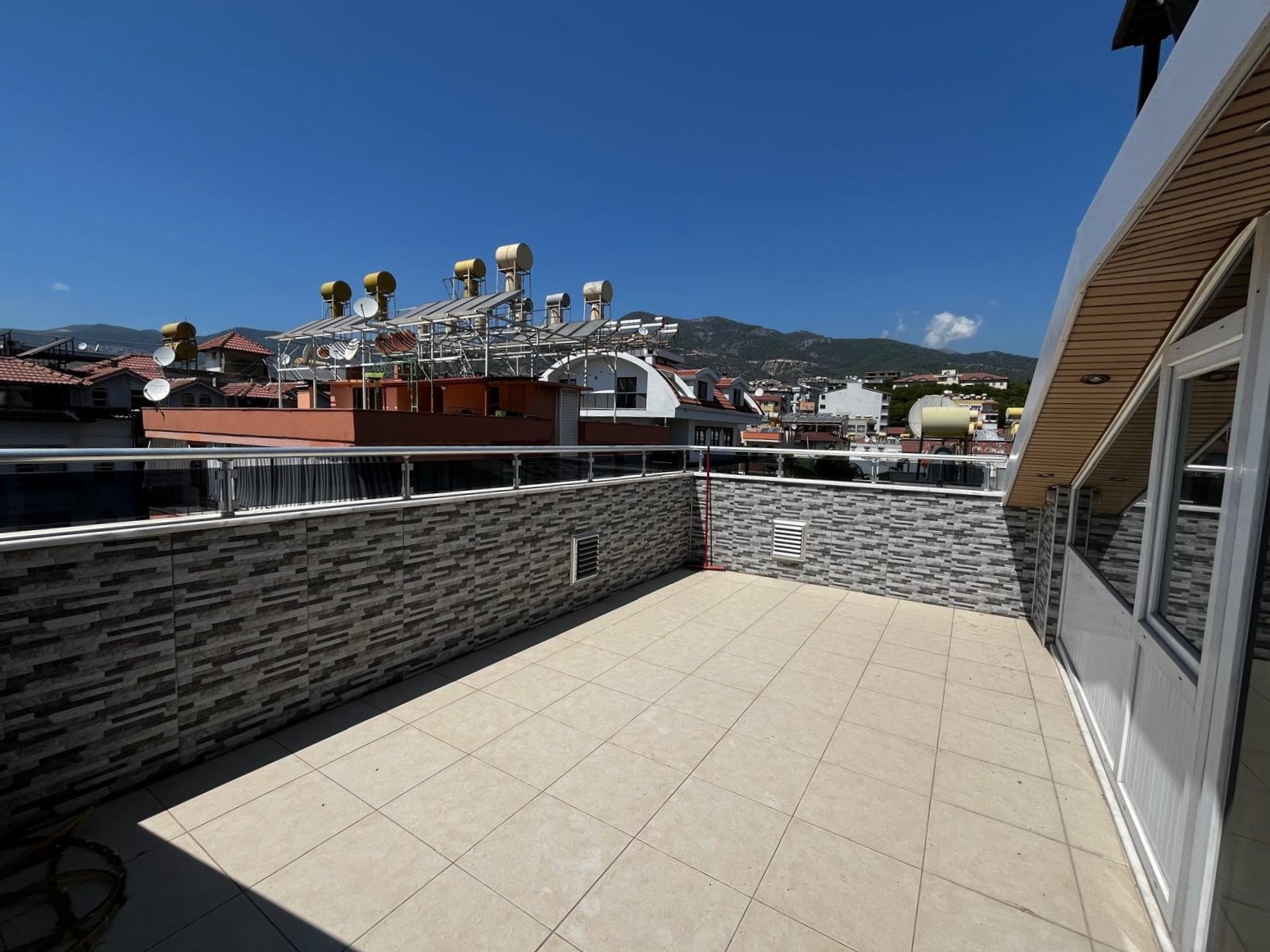 Alanya’da satışa sunulan geniş terasta taş kaplı parapet, şehir çatıları ve dağ yamacı