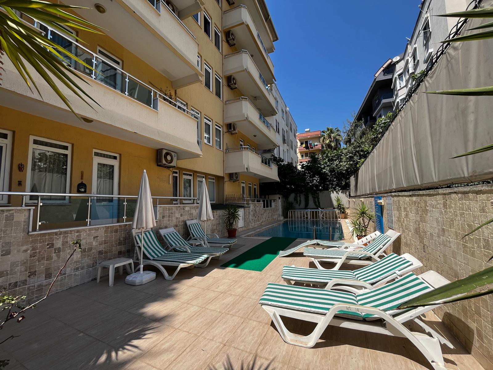 Alanya’da taş kaplı duvar boyunca sıralanan çizgili şezlonglar ve açık havuz dinlenme alanı