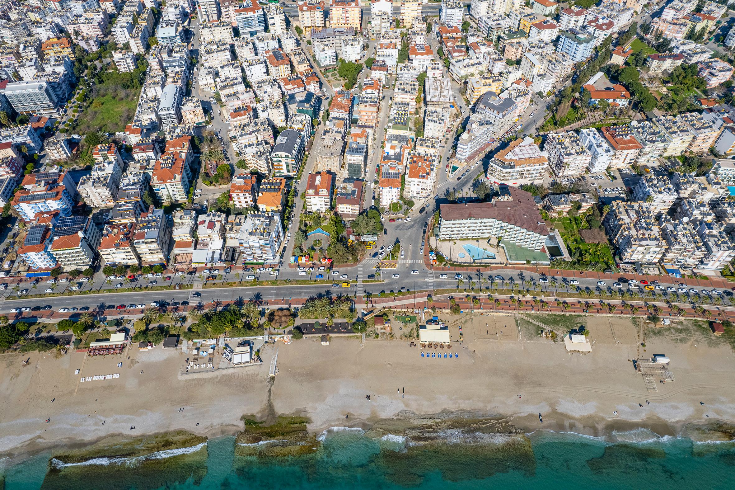 Alanya’da satıştaki konutların çevresinde dalgalı turkuaz deniz, geniş plaj ve sahil yolu