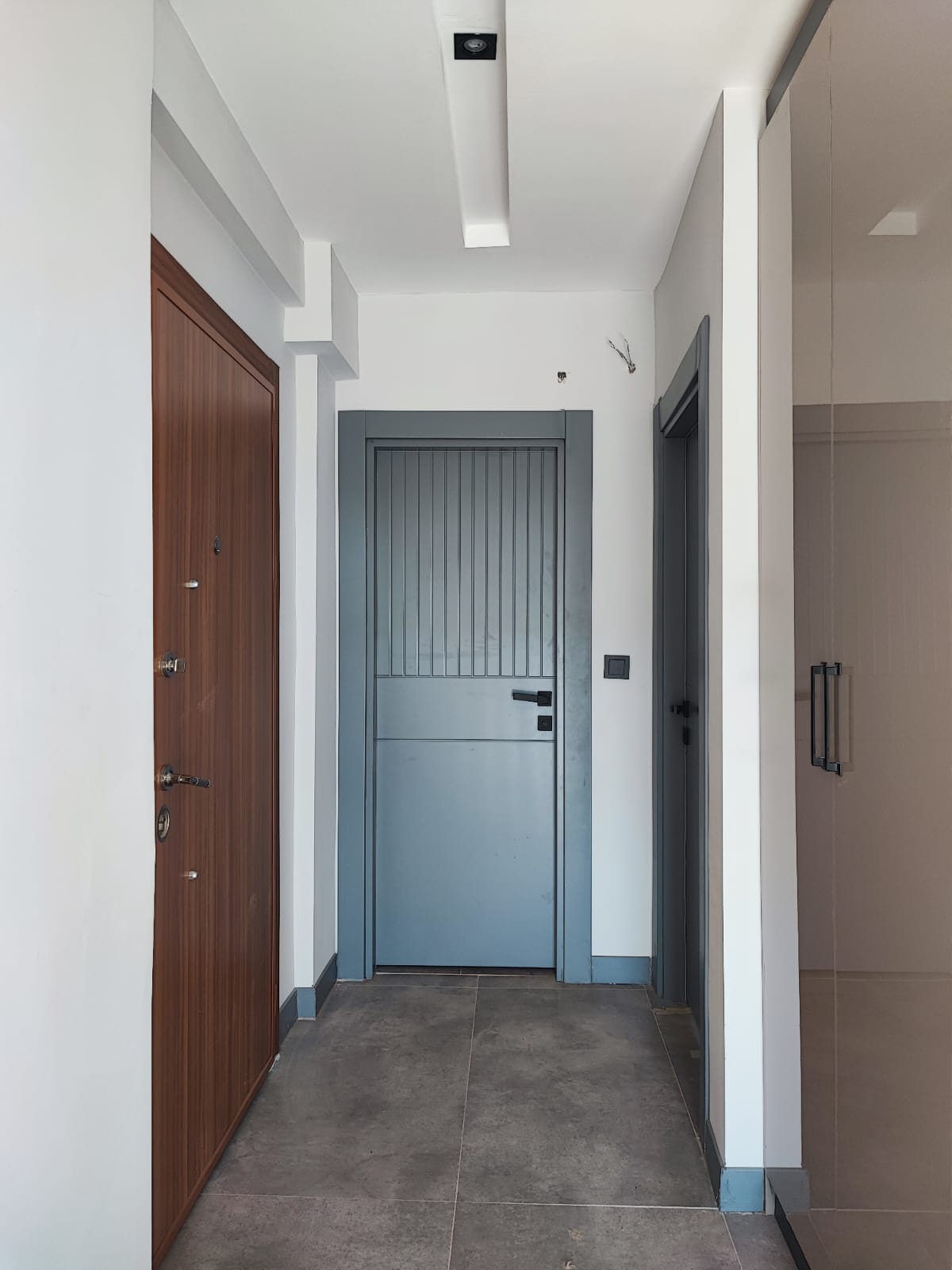 Entry hall with a beige built-in wardrobe, gray door and dark gray floor tiles