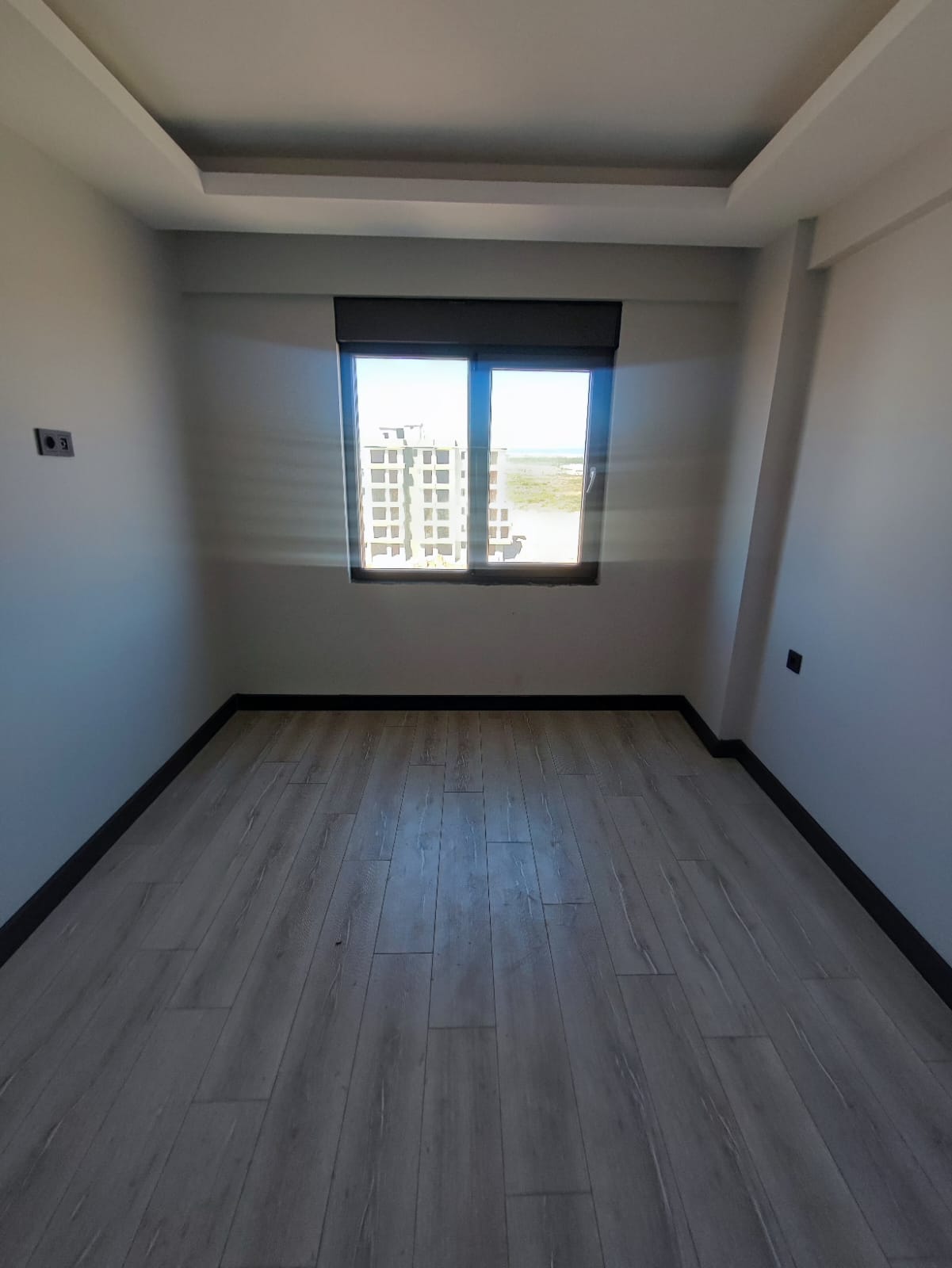 Narrow bedroom in a flat in Antalya with a dark-framed window facing neighboring buildings
