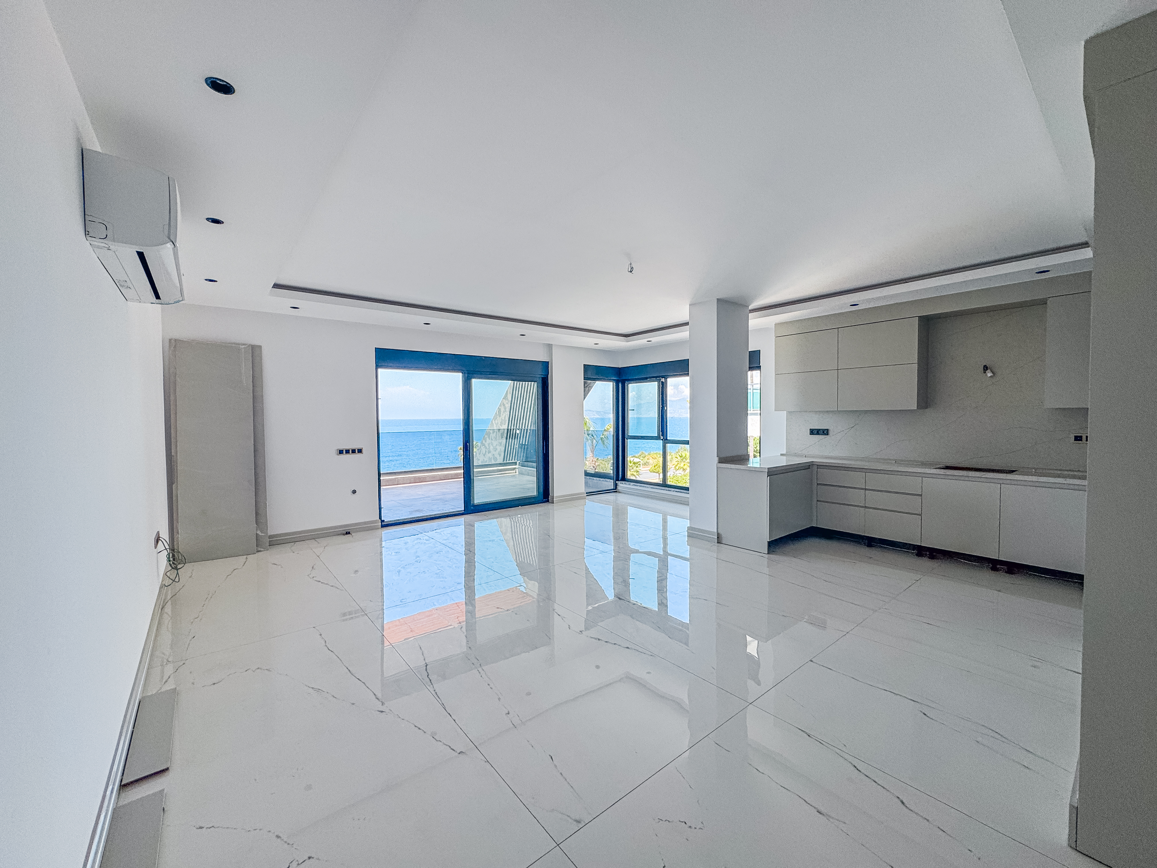 Satılık 4+1 dairenin mutfaklı salonunda bej dolaplar, balkon çıkışı ve deniz manzarası