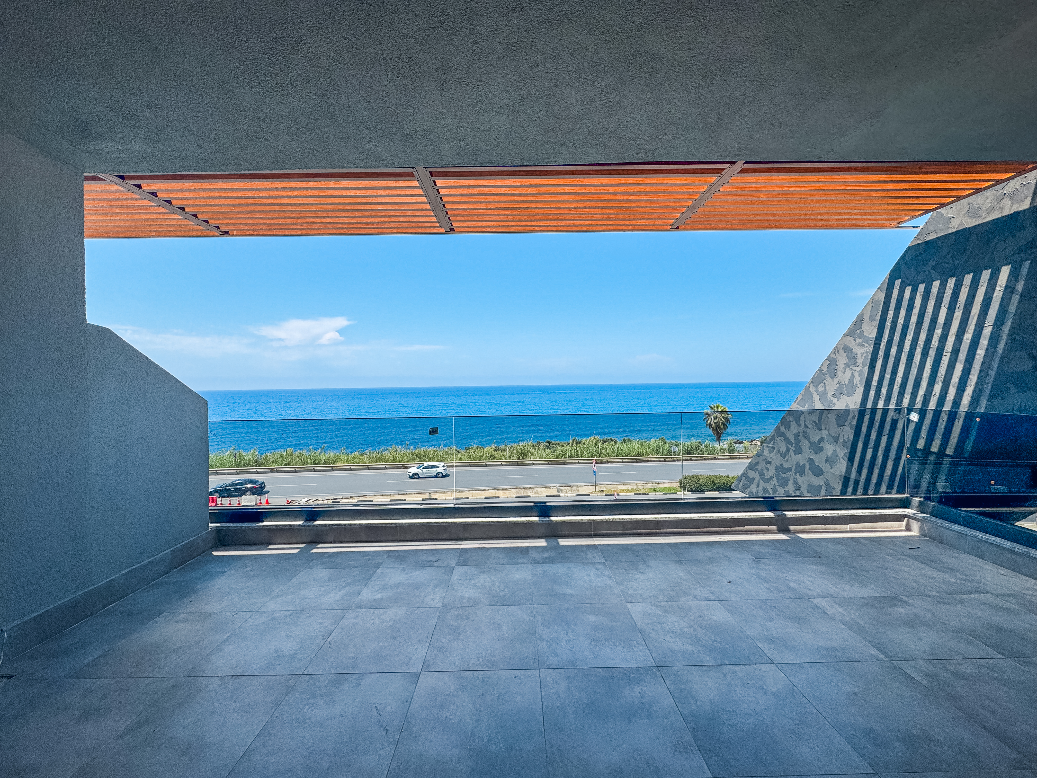 Sahilde satılık konutun kapalı terasında cam korkuluk, ahşap pergola ve panoramik deniz manzarası