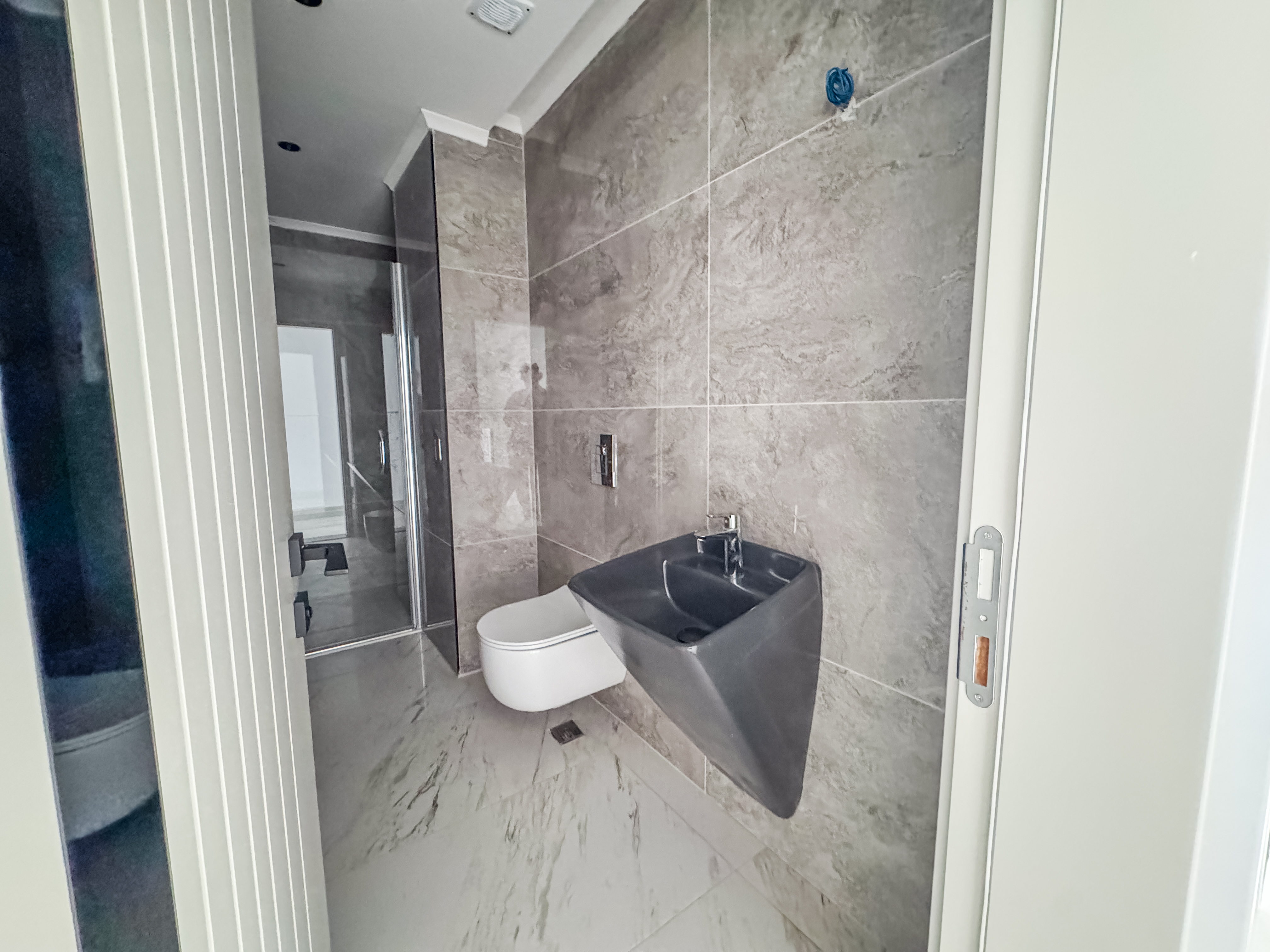 Ev banyosunda aynalı duvar, asılı koyu gri lavabo ve taş görünümlü gri kahverengi fayanslar