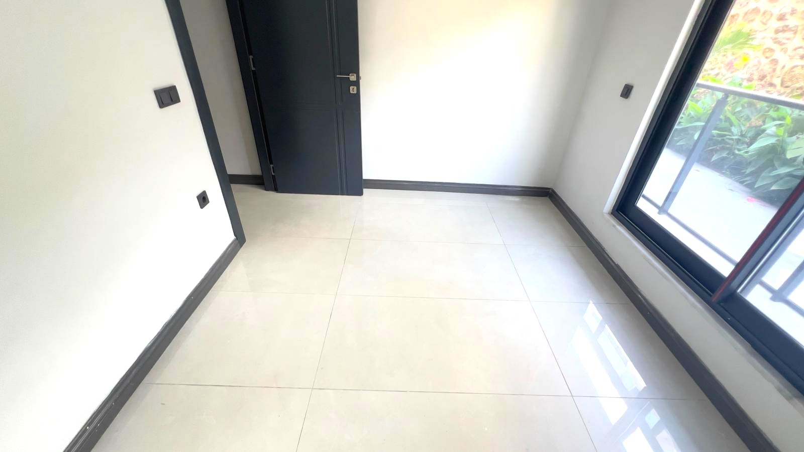 Alanya’daki dairenin yatak odasında panoramik pencere, siyah iç kapı ve dışarıdaki balkon korkuluğu