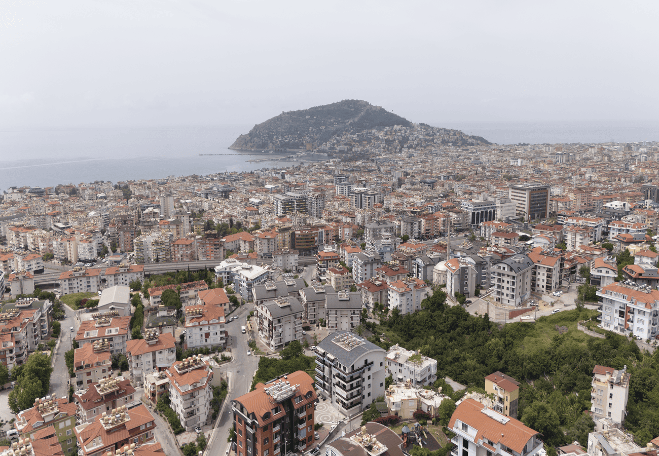 Deniz kıyısındaki yeşil tepe, kırmızı kiremitli çatılar ve satılık dairelerin bulunduğu yoğun kent dokusu