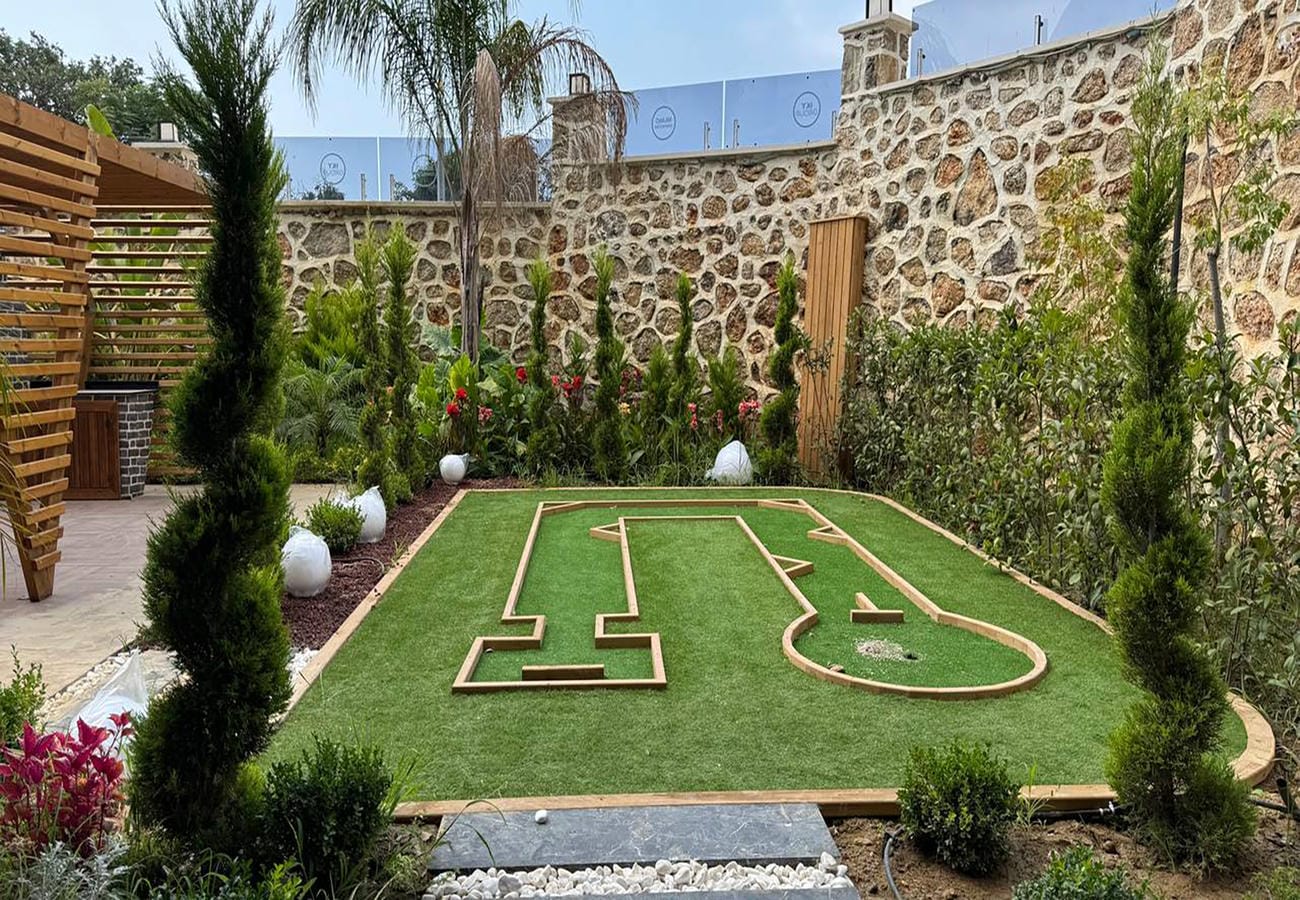 Türkiye’de mini golf alanında bayraklı delik, ahşap saha kenarları ve yüksek taş duvar