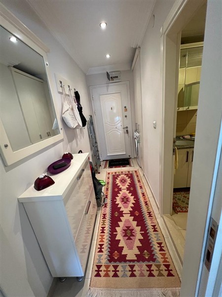 1+1 dairenin uzun antre koridorunda kabartmalı beyaz kapı, ayna ve desenli yolluk