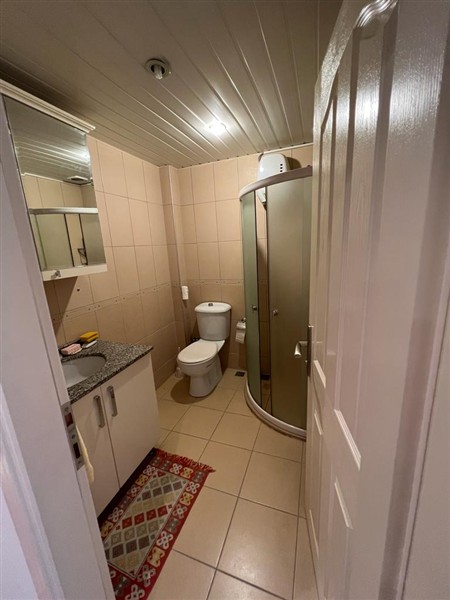 Alanya’daki banyoda buzlu camlı köşe duş kabini, oval lavabo ve aynalı dolap