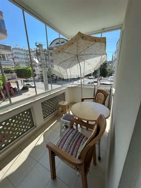 Alanya’daki satılık 1+1 dairenin camlı balkonunda yuvarlak masa, iki ahşap sandalye ve şemsiye