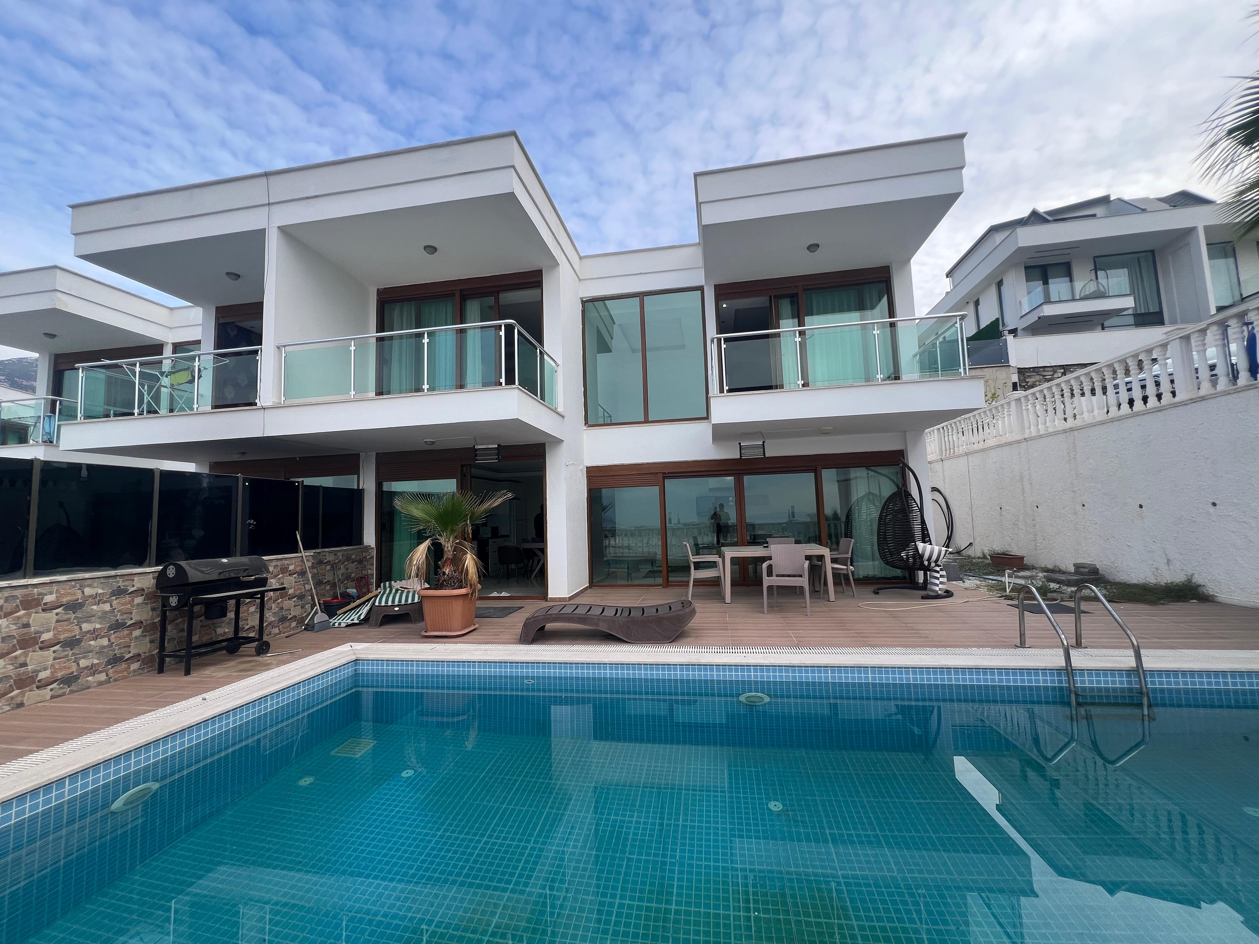 White two-storey villa facade with glass balconies and a pool in Kargicak, Turkey