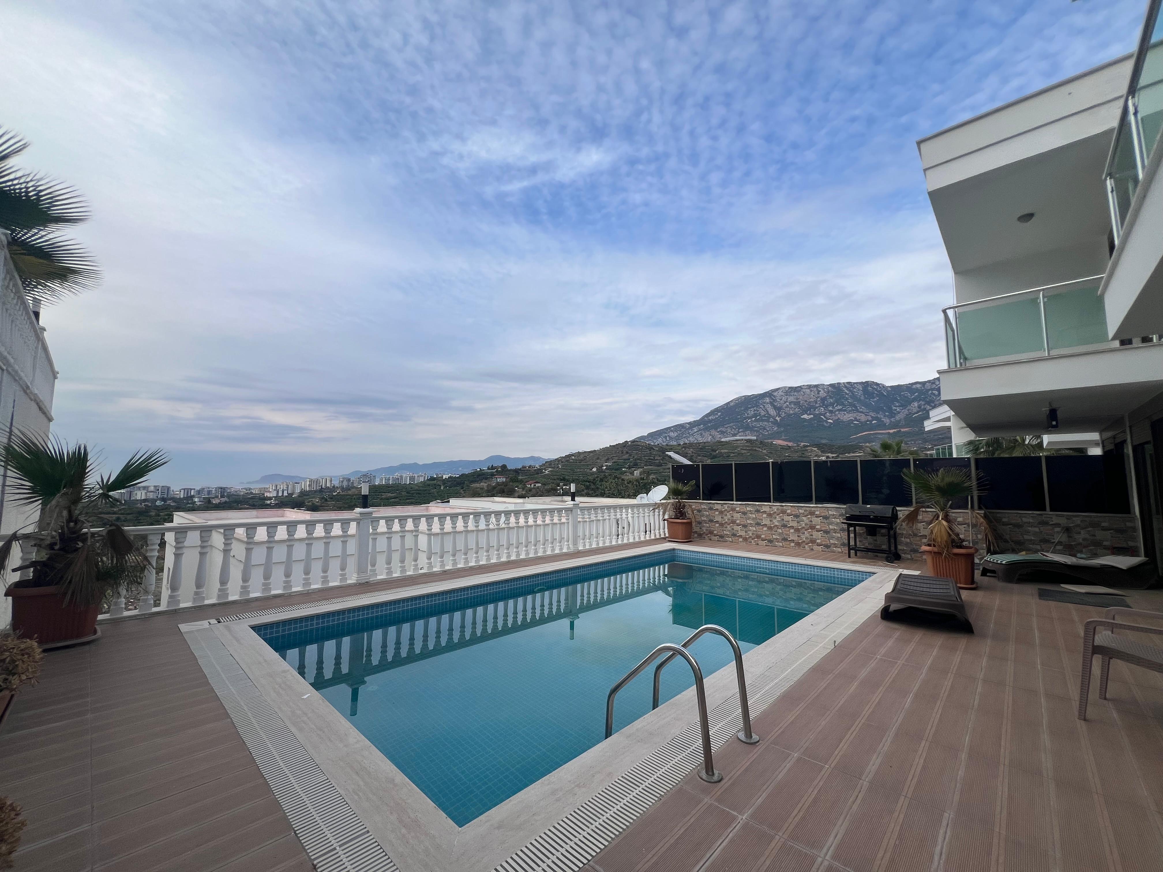 Rectangular pool with steps beside a villa’s side facade and mountain views in Kargicak for sale