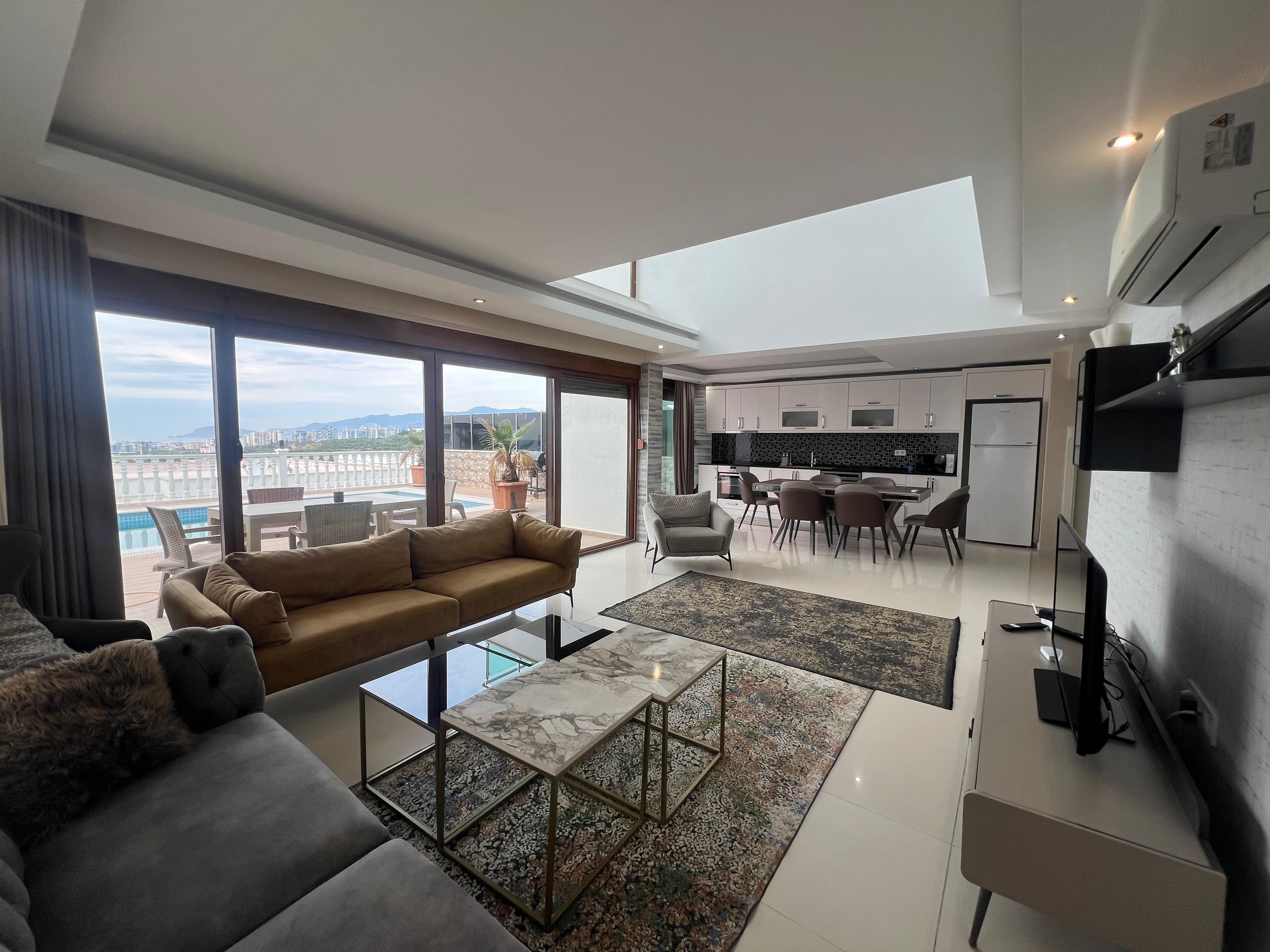 Kitchen-living room with an L-shaped gray sofa, dining area and panoramic glazing