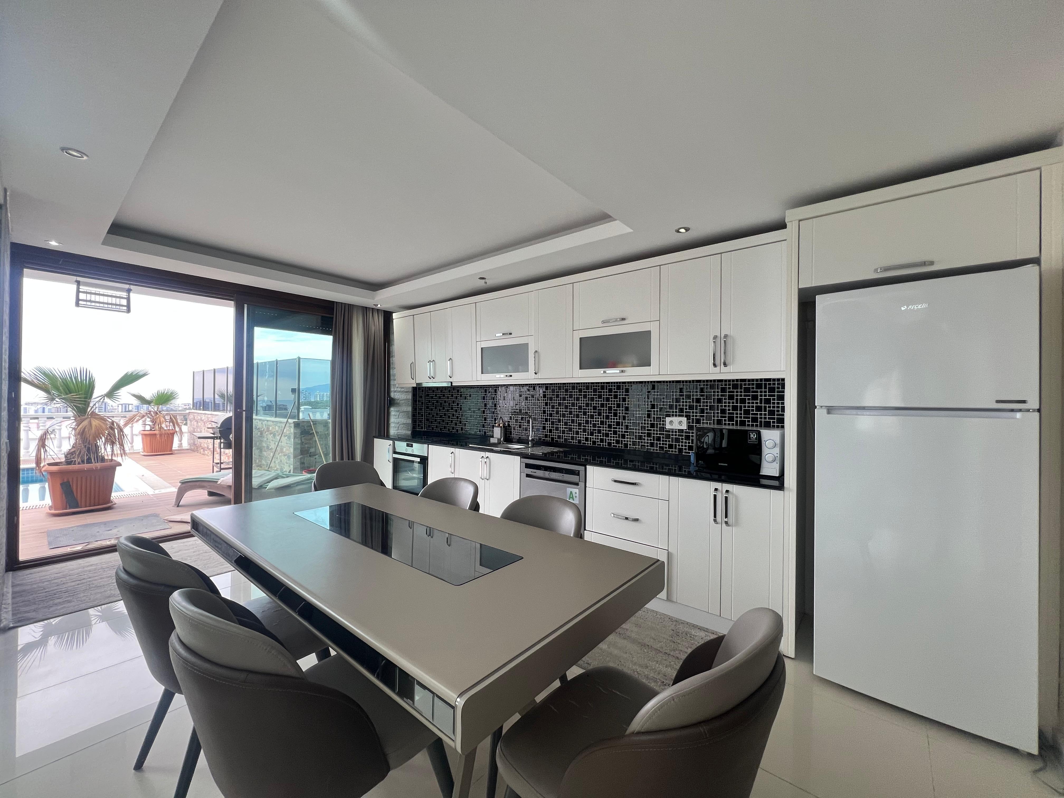 Kitchen with white cabinetry, an island hob and black mosaic backsplash in Kargicak