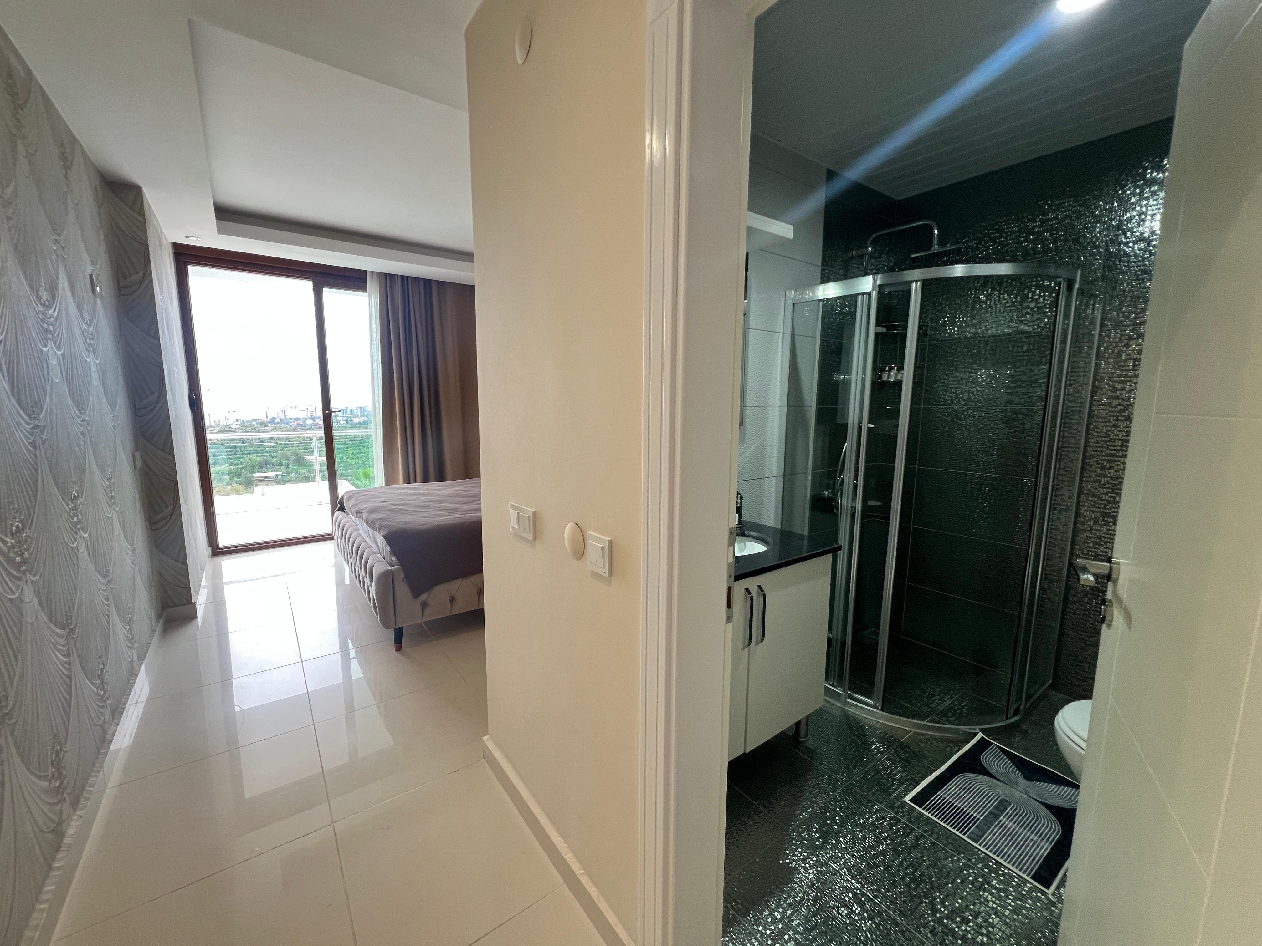 Bathroom with a corner shower, black mosaic tiles and a bedroom beyond in a detached home