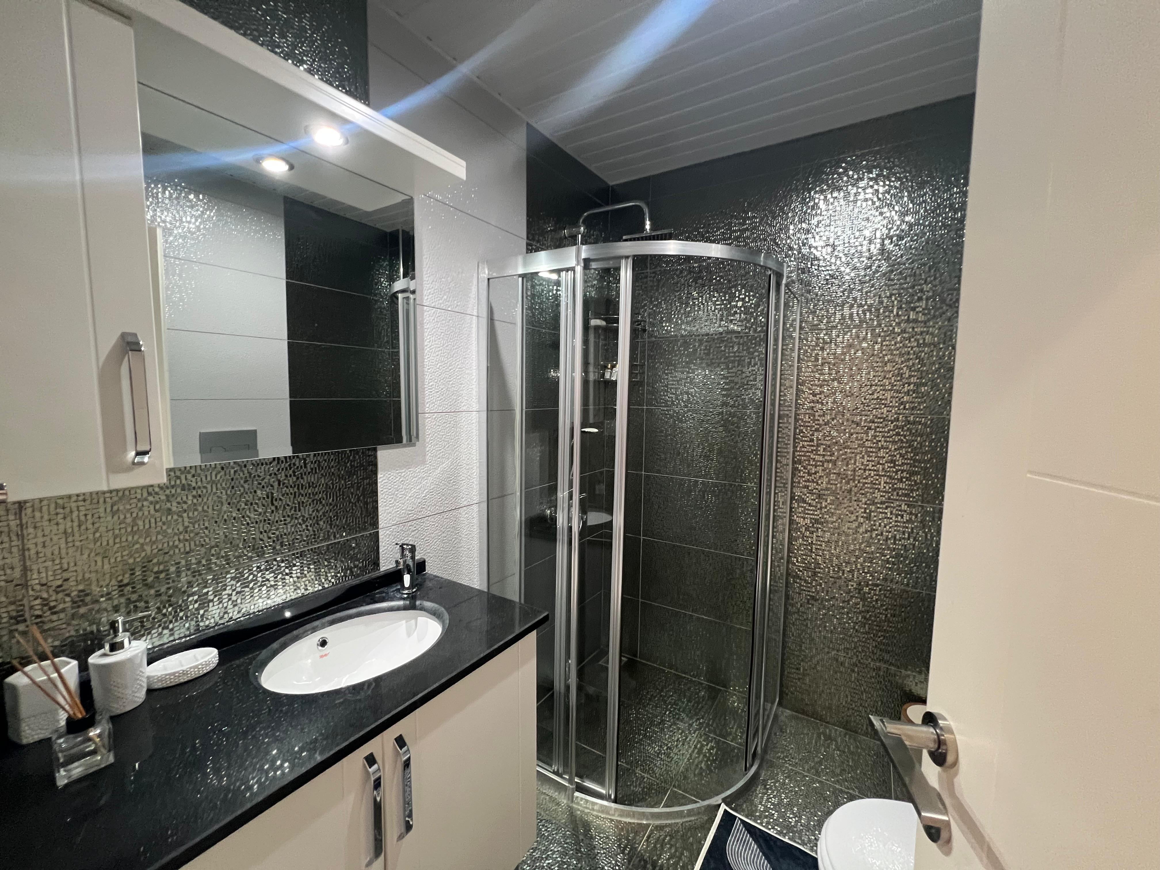 Bathroom with a corner shower, black mosaic tiles and a wall-mounted cabinet in Kargicak