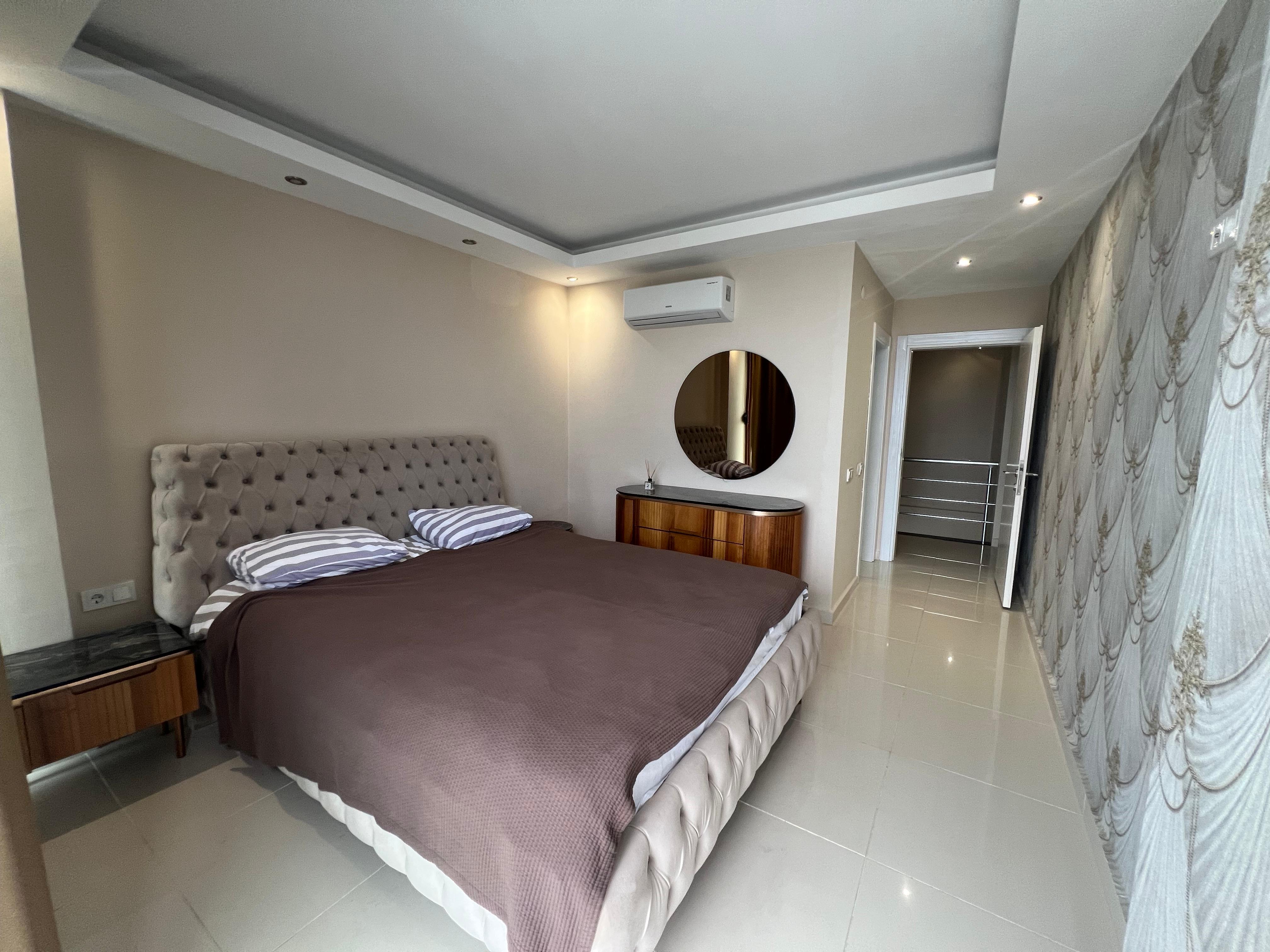 Bedroom with an upholstered double bed, chest of drawers and panoramic window in a house