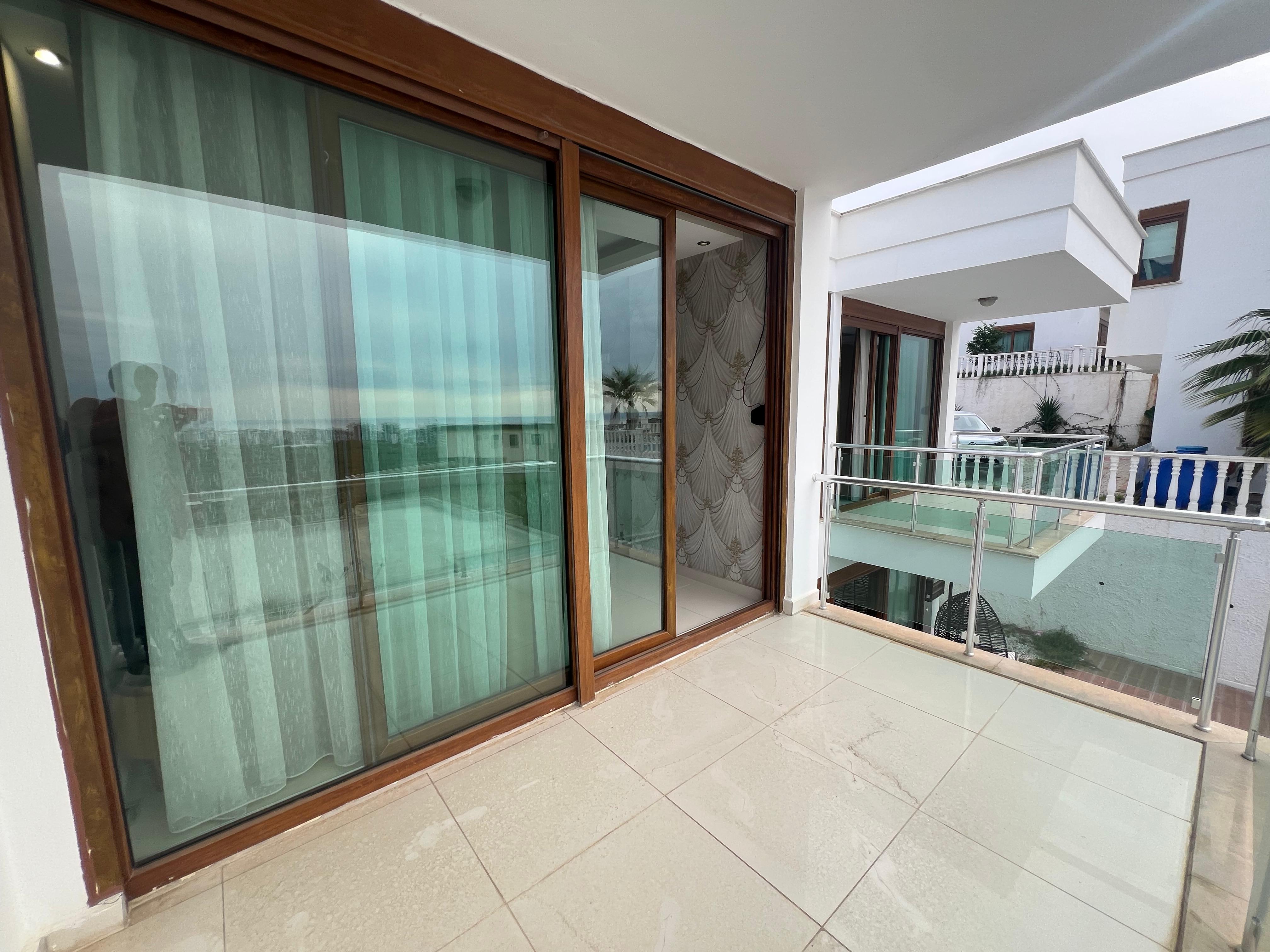 Terrace with sliding glass doors and glass railings beside neighboring white buildings in Kargicak