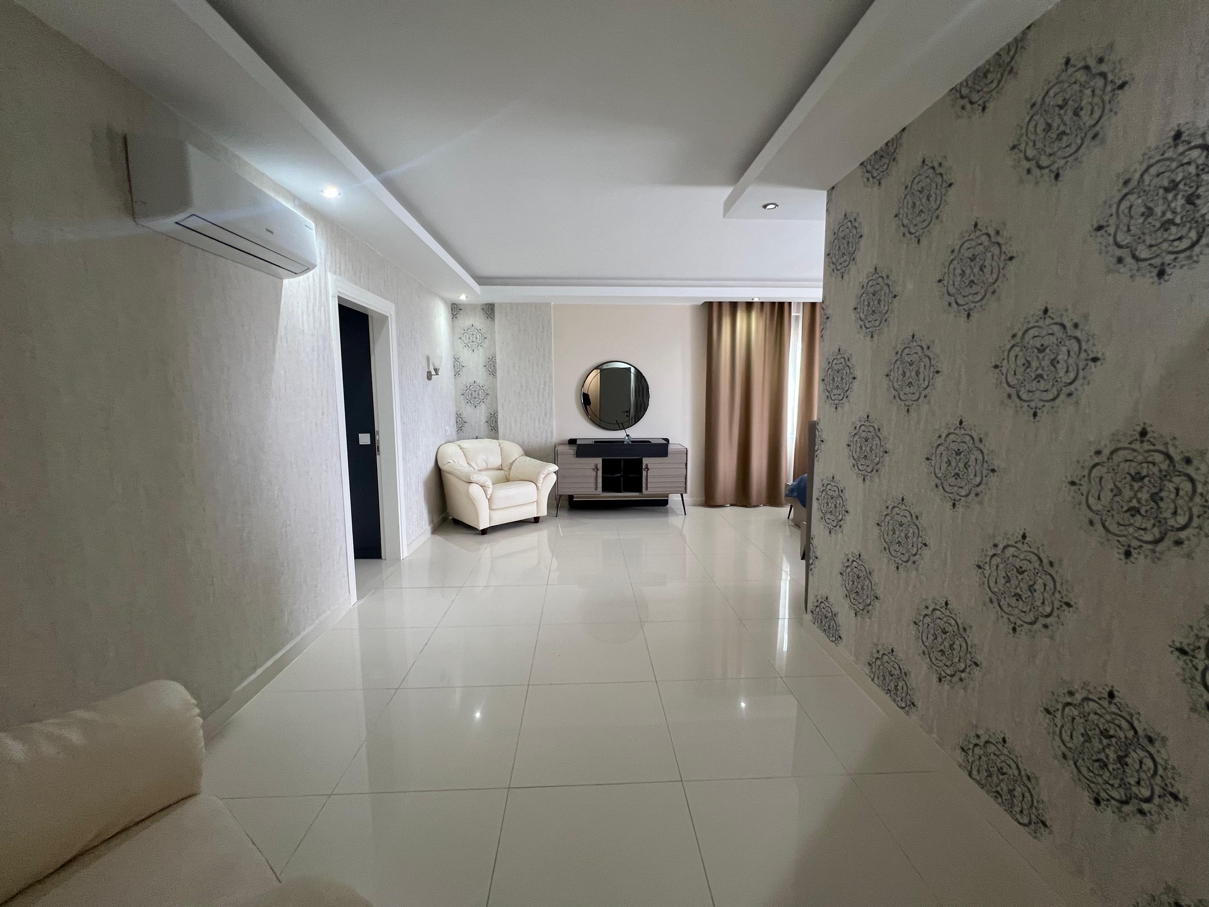 Living room with a white armchair and round wall mirror in a house available for sale