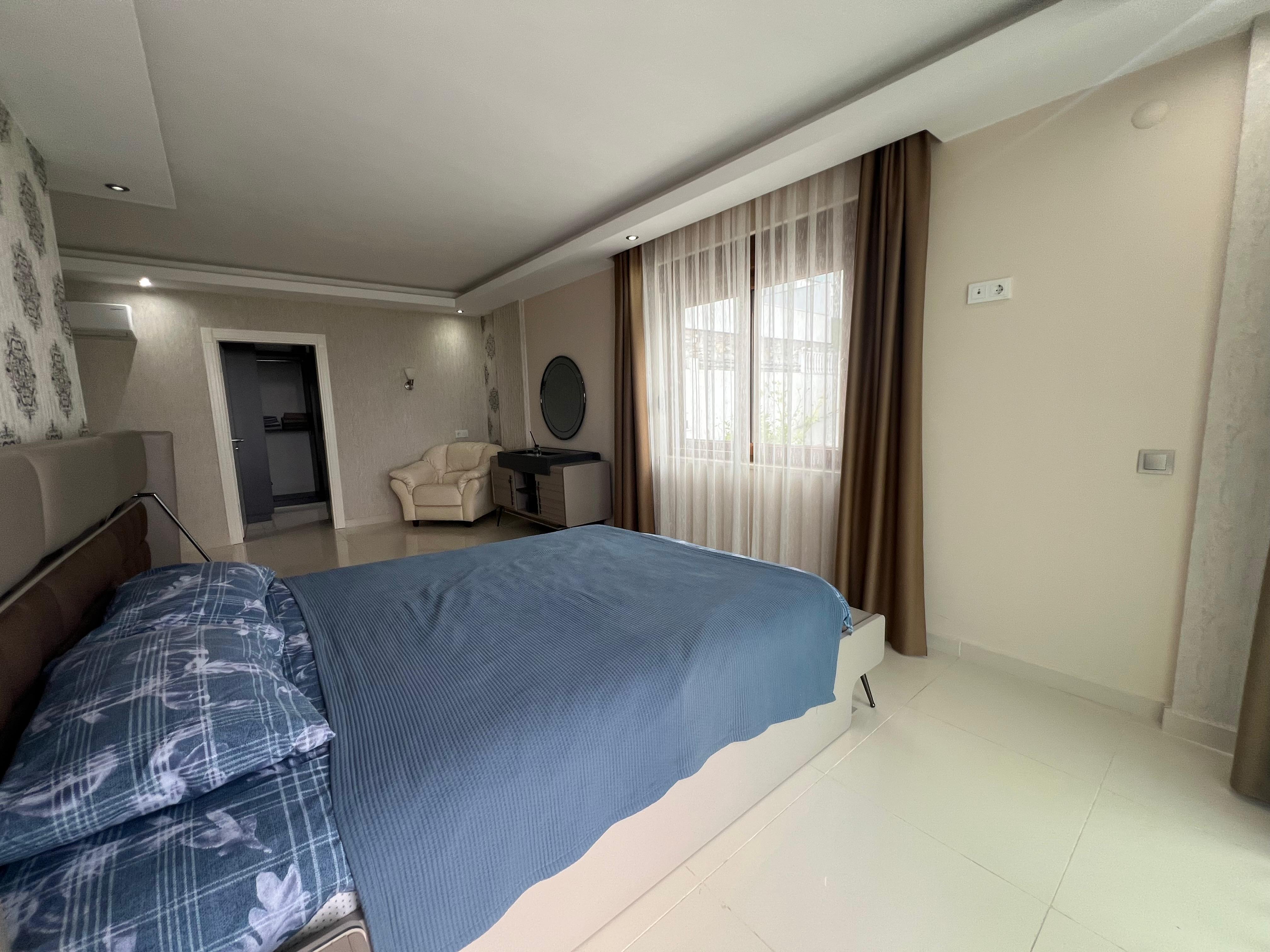 Bedroom with a double bed, blue coverlet and round mirror above the chest in a villa