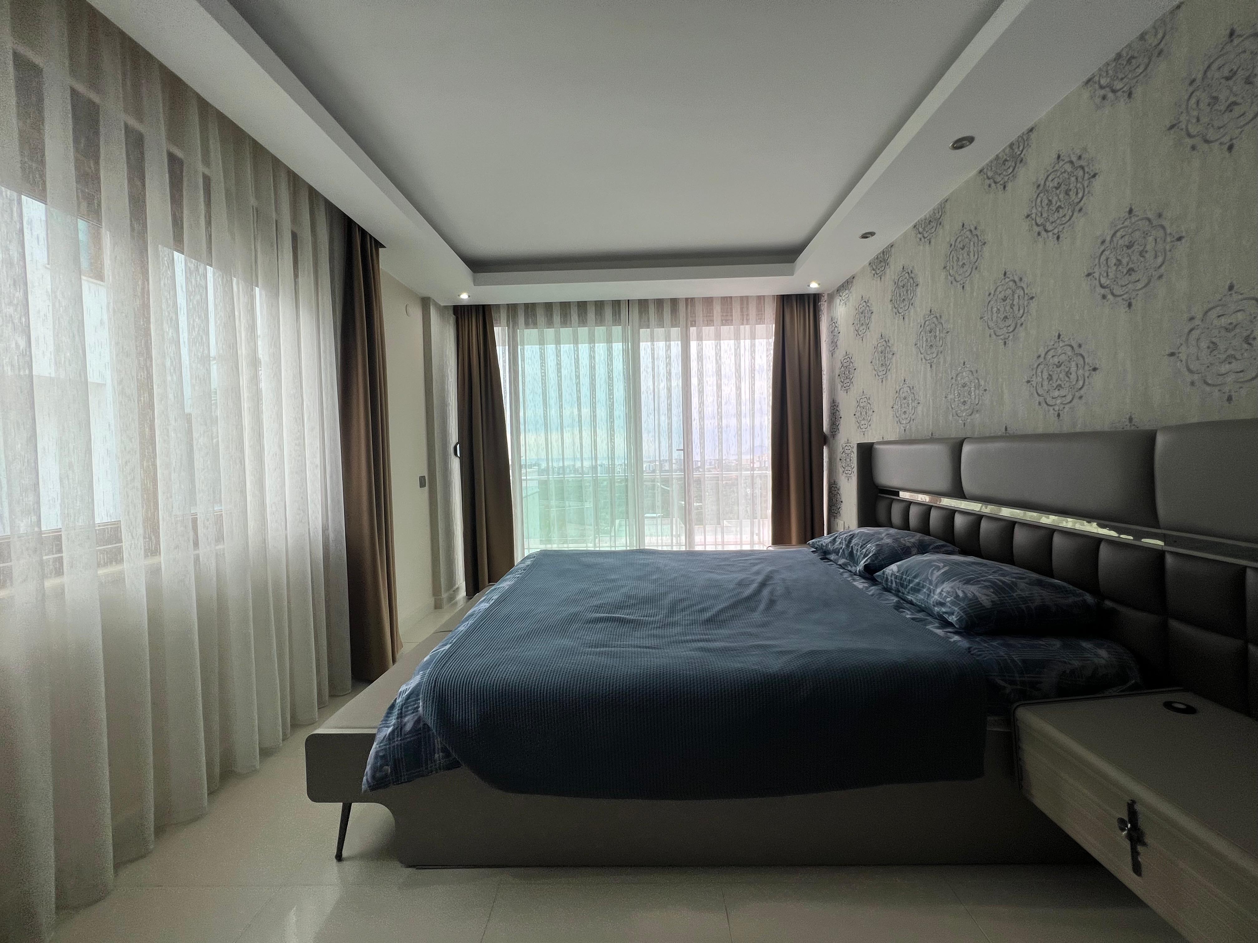 Bedroom with a dark upholstered headboard, blue coverlet and patterned wallpaper in Kargicak