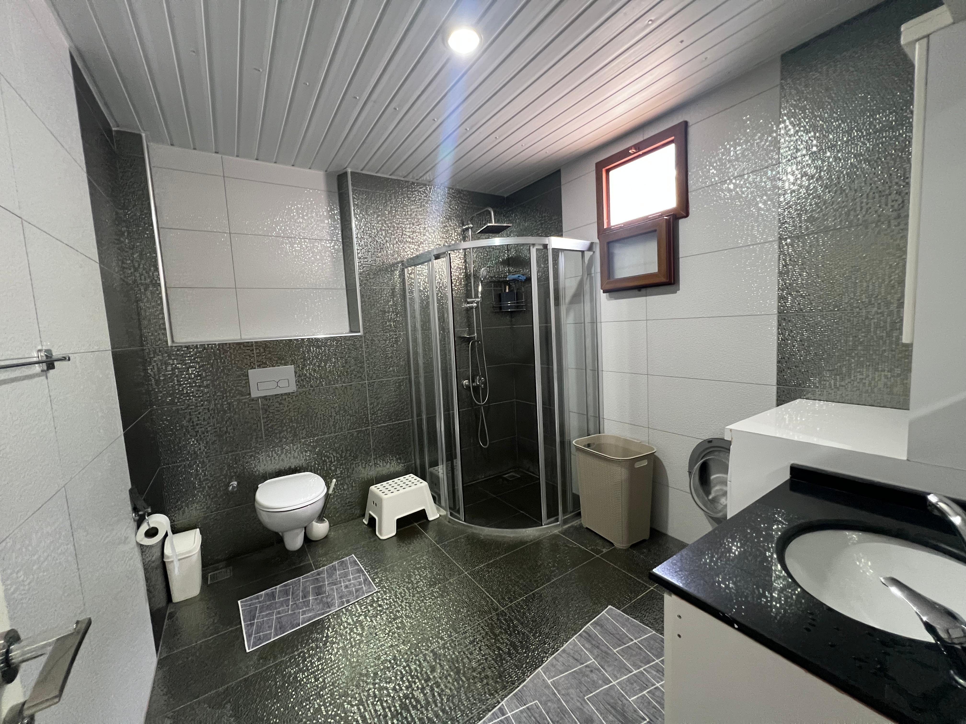 Bathroom with a corner shower, washing machine and gray-white mosaic wall cladding in a house