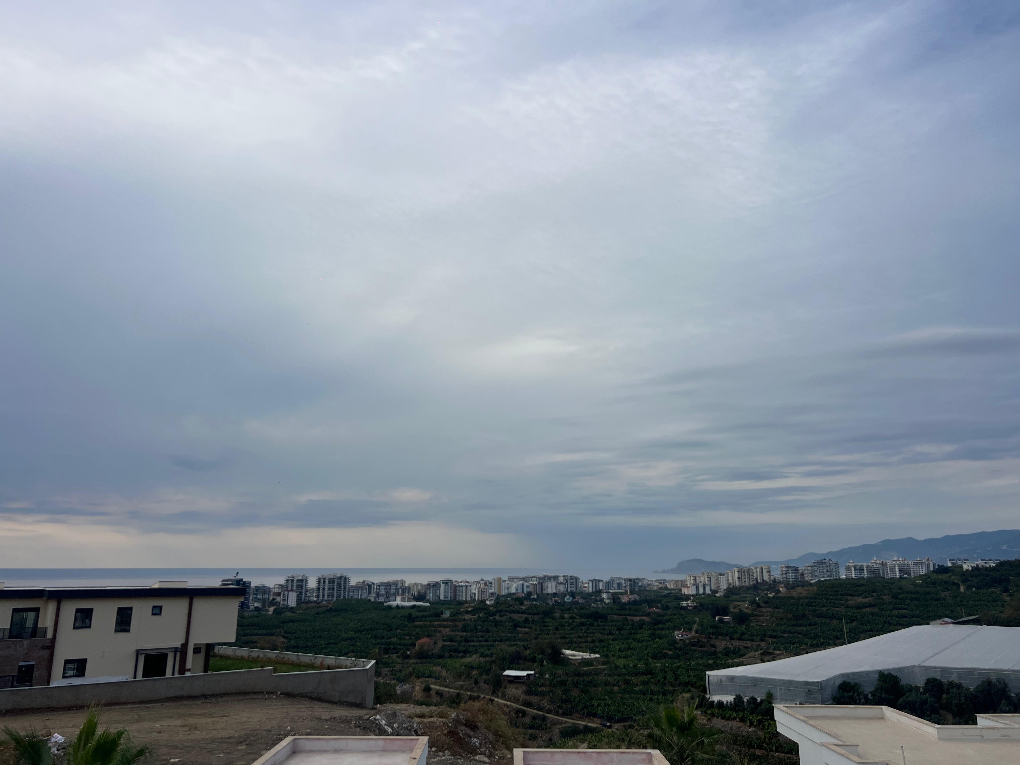 Panoramic view of city buildings, green agricultural land and a mountain ridge under cloudy skies