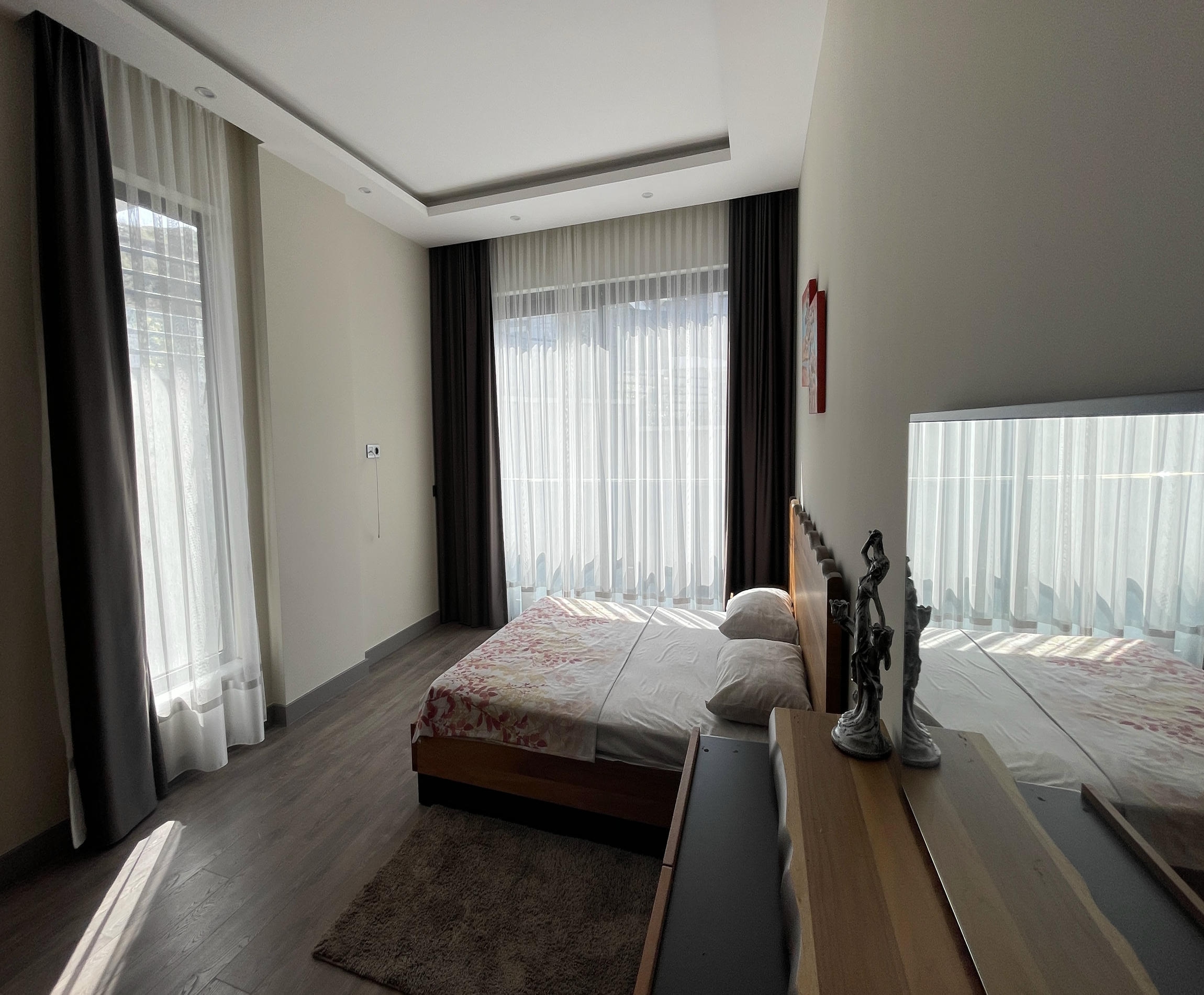 Tekstil başlıklı yatak bulunan yatak odasında iki duvarda panoramik pencereler villa içinde