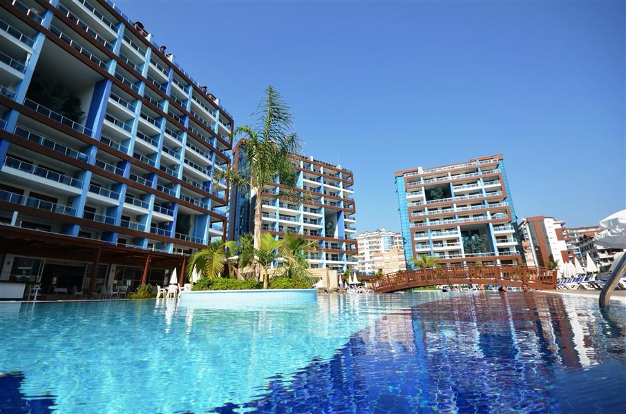 Büyük açık havuz ve ahşap köprü Türkiye’de kiralık dairelerin bulunduğu sitede palmiyelerle çevrili
