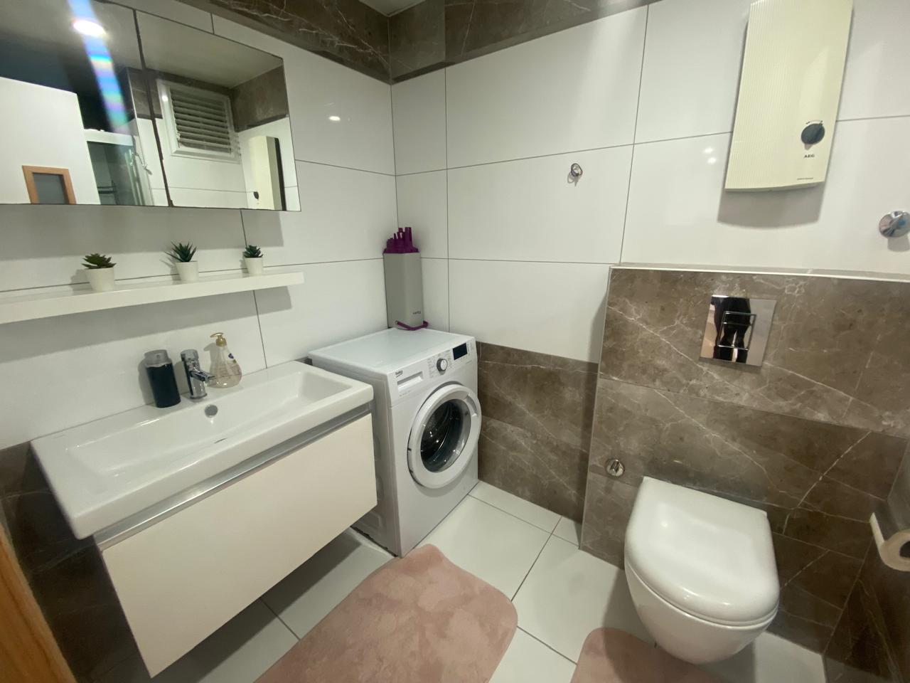 Çift kişilik yataklı dairenin banyosunda lavabo, aynalı dolap ve çamaşır makinesi yer alıyor
