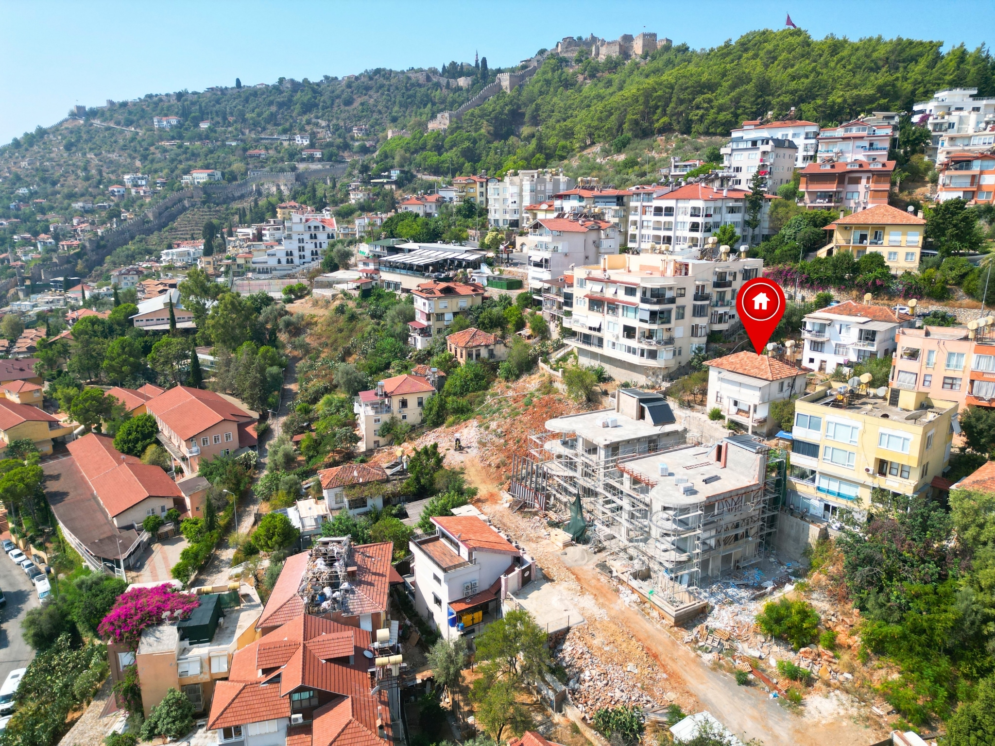 A green hillside with fortress walls and a red-tiled villa among trees in Alanya, Turkey