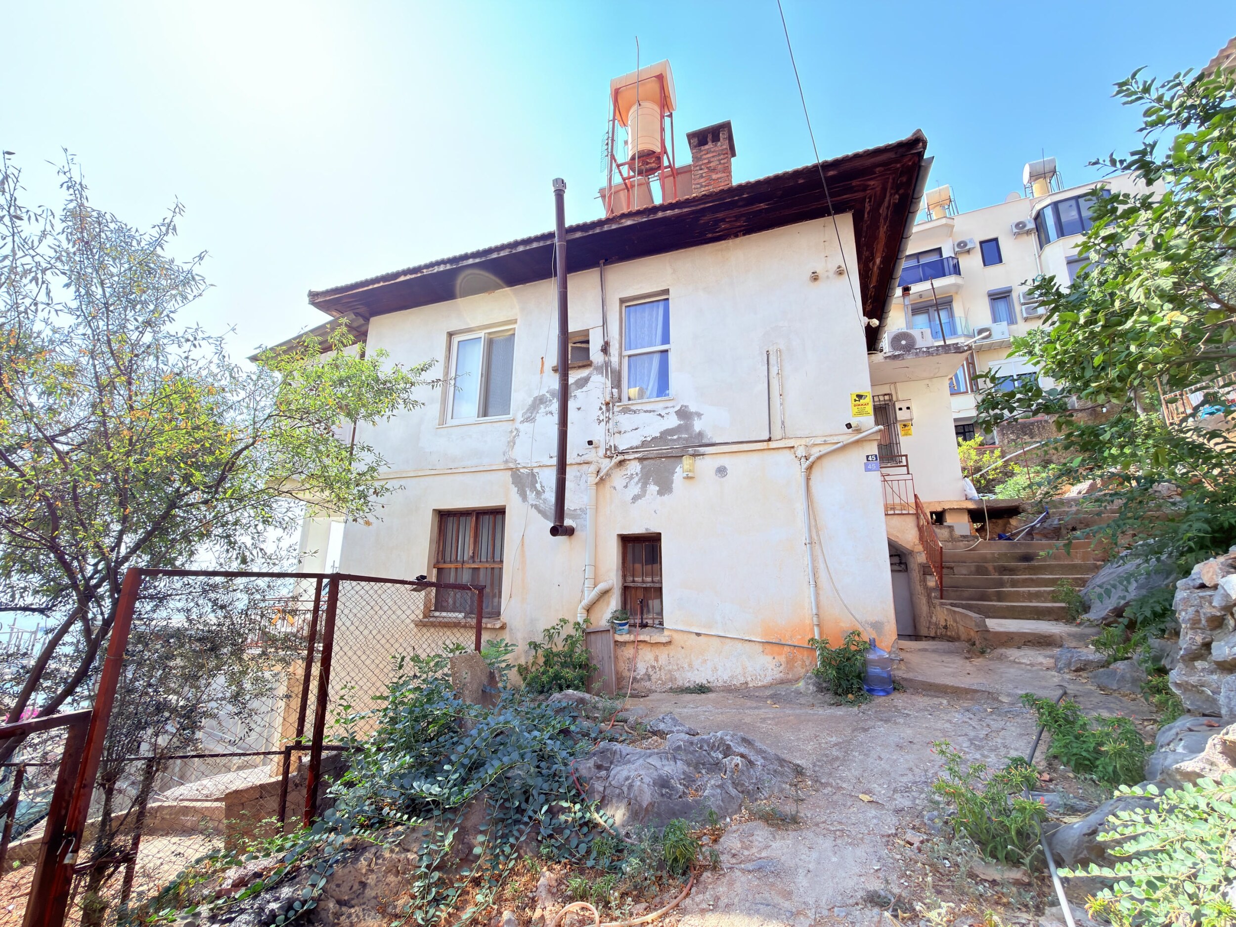An aged two-story villa with a terracotta roof and stone steps in Alanya for sale