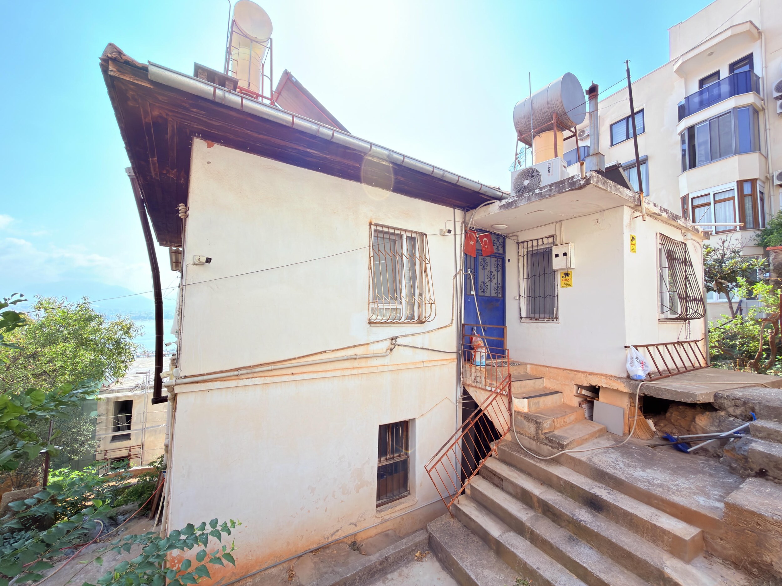 The side of an old home with a blue door, concrete steps and metal railings
