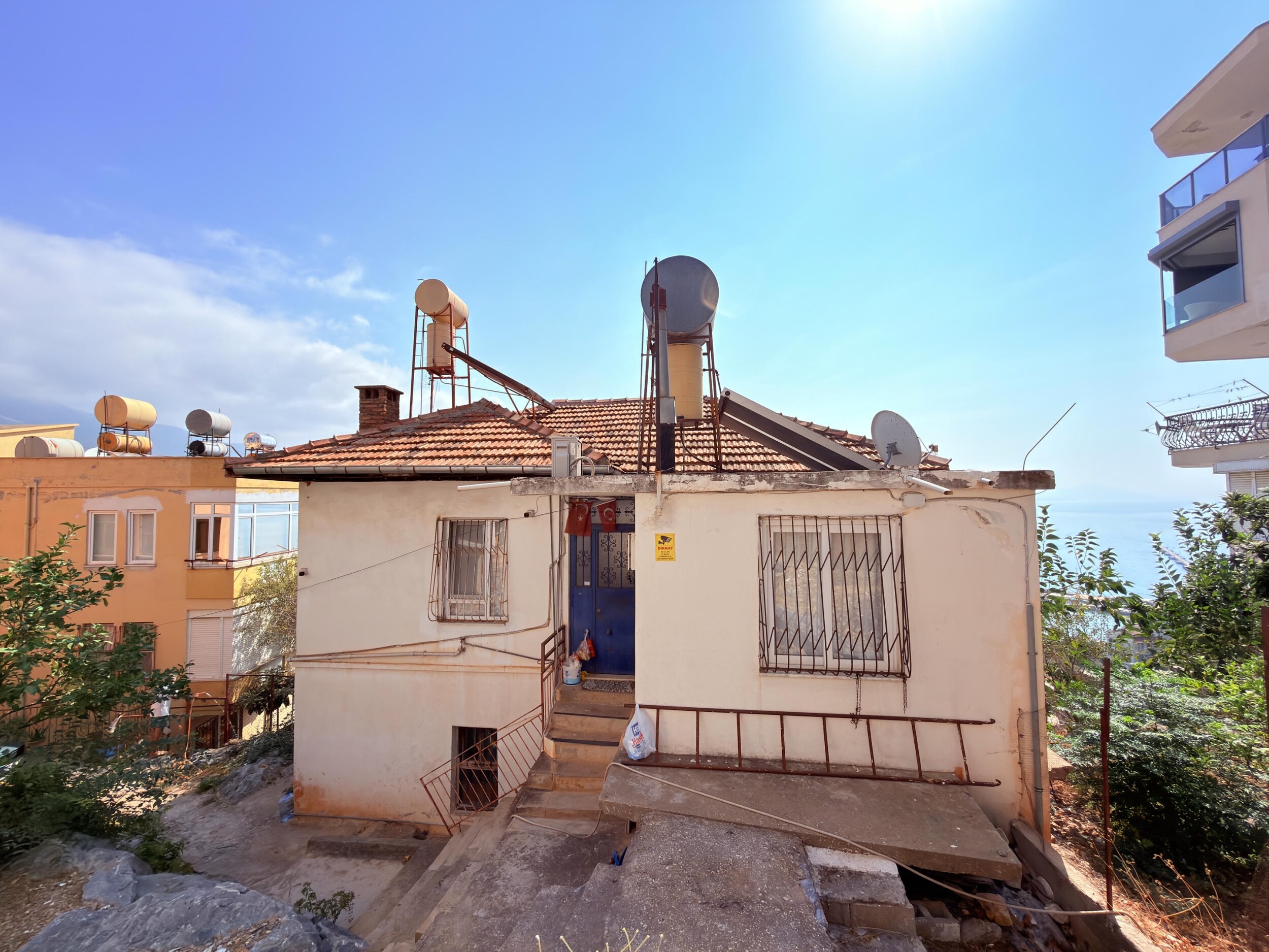 A front-facing single-story villa with a blue door and neighboring homes in Alanya