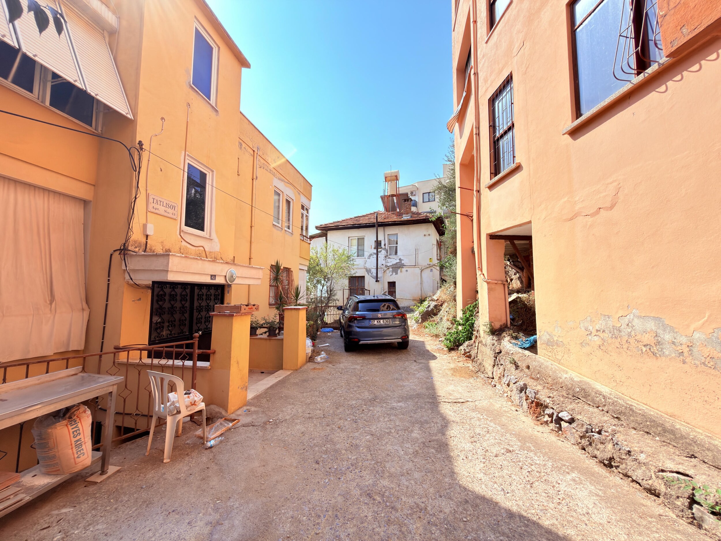 A narrow asphalt street between orange residential homes leads to a detached home