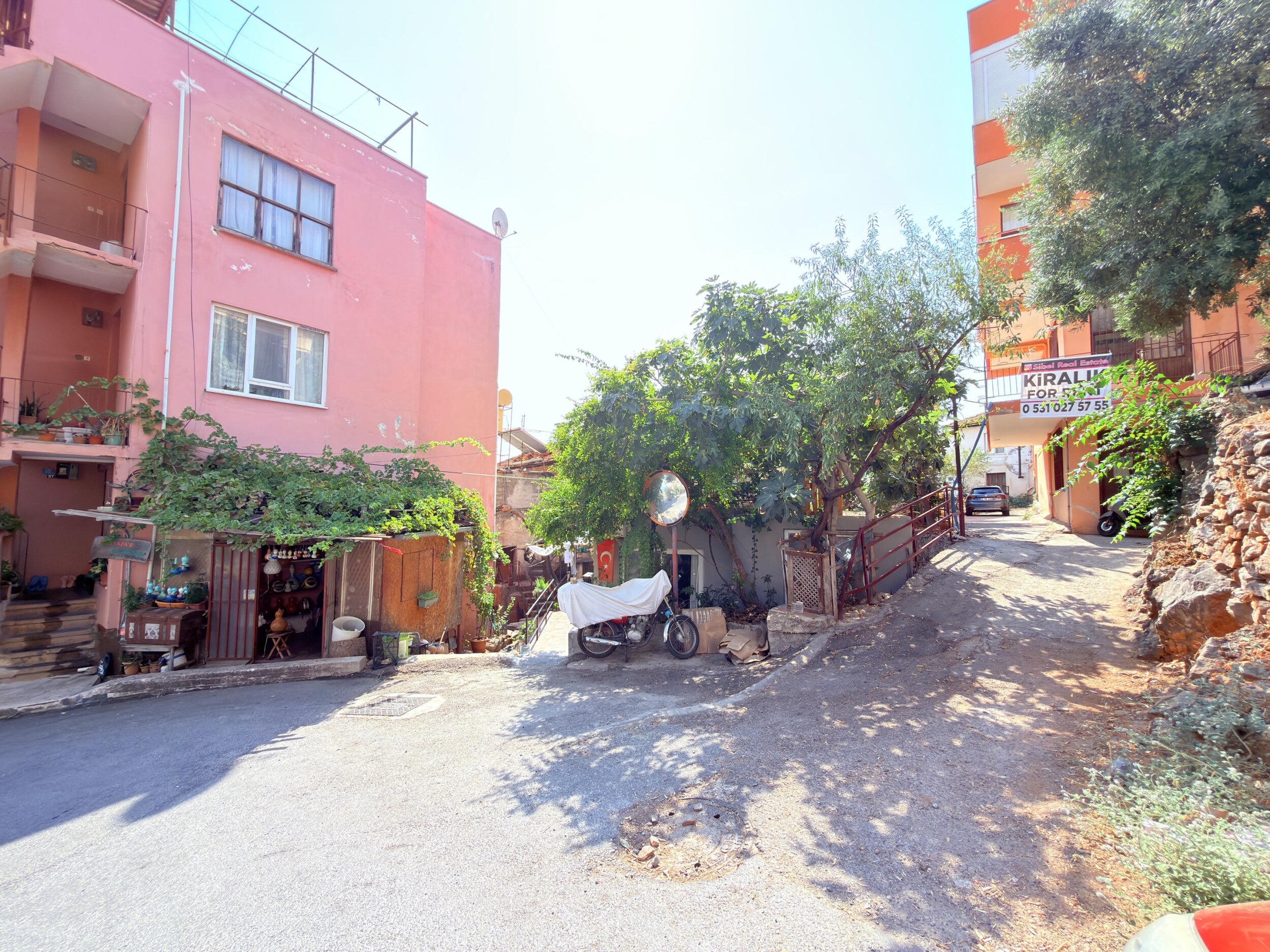 A residential street intersection with a pink building, retaining wall and steep incline