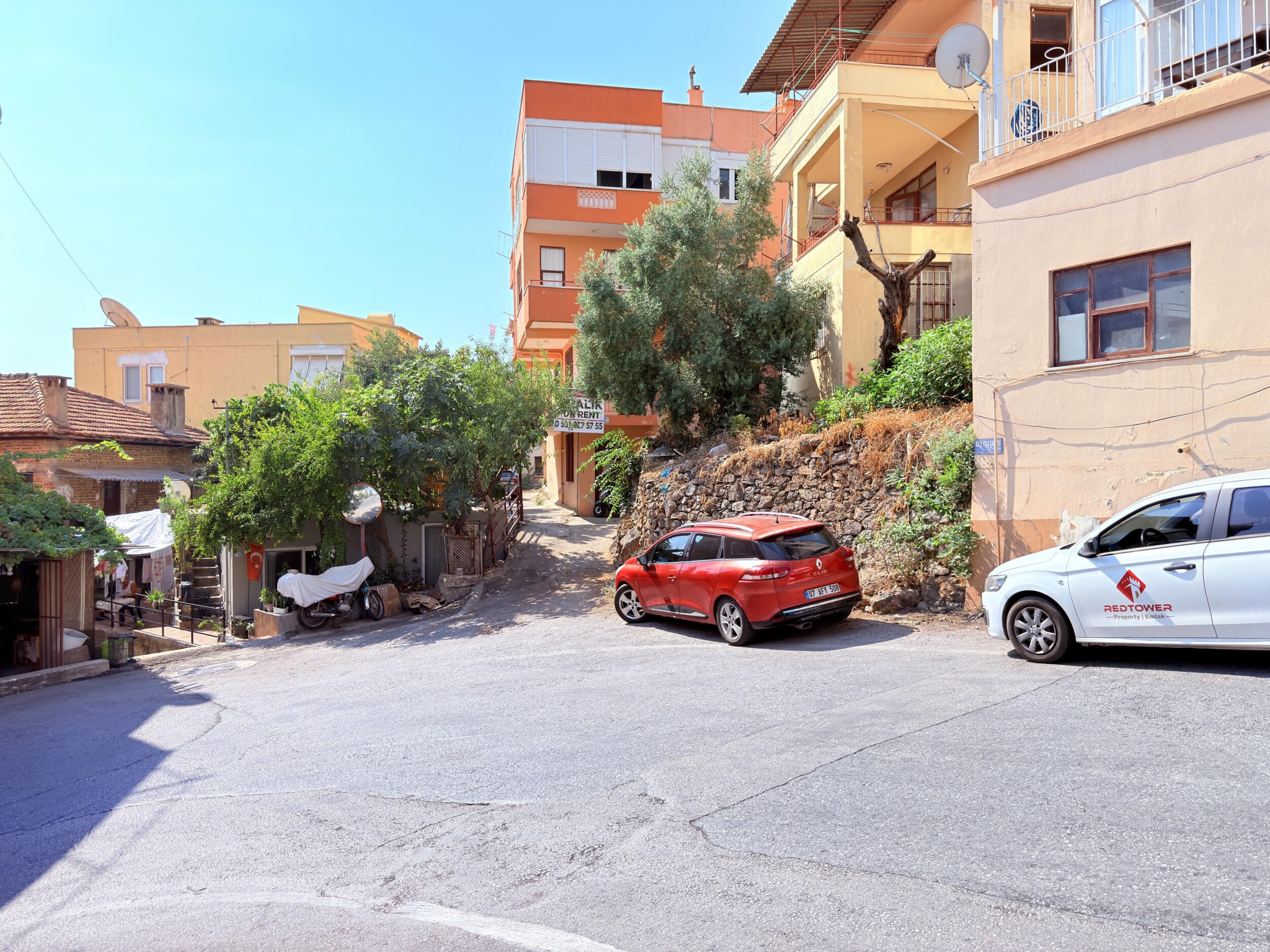 An asphalt street between orange and beige homes leads to a villa for sale in Alanya