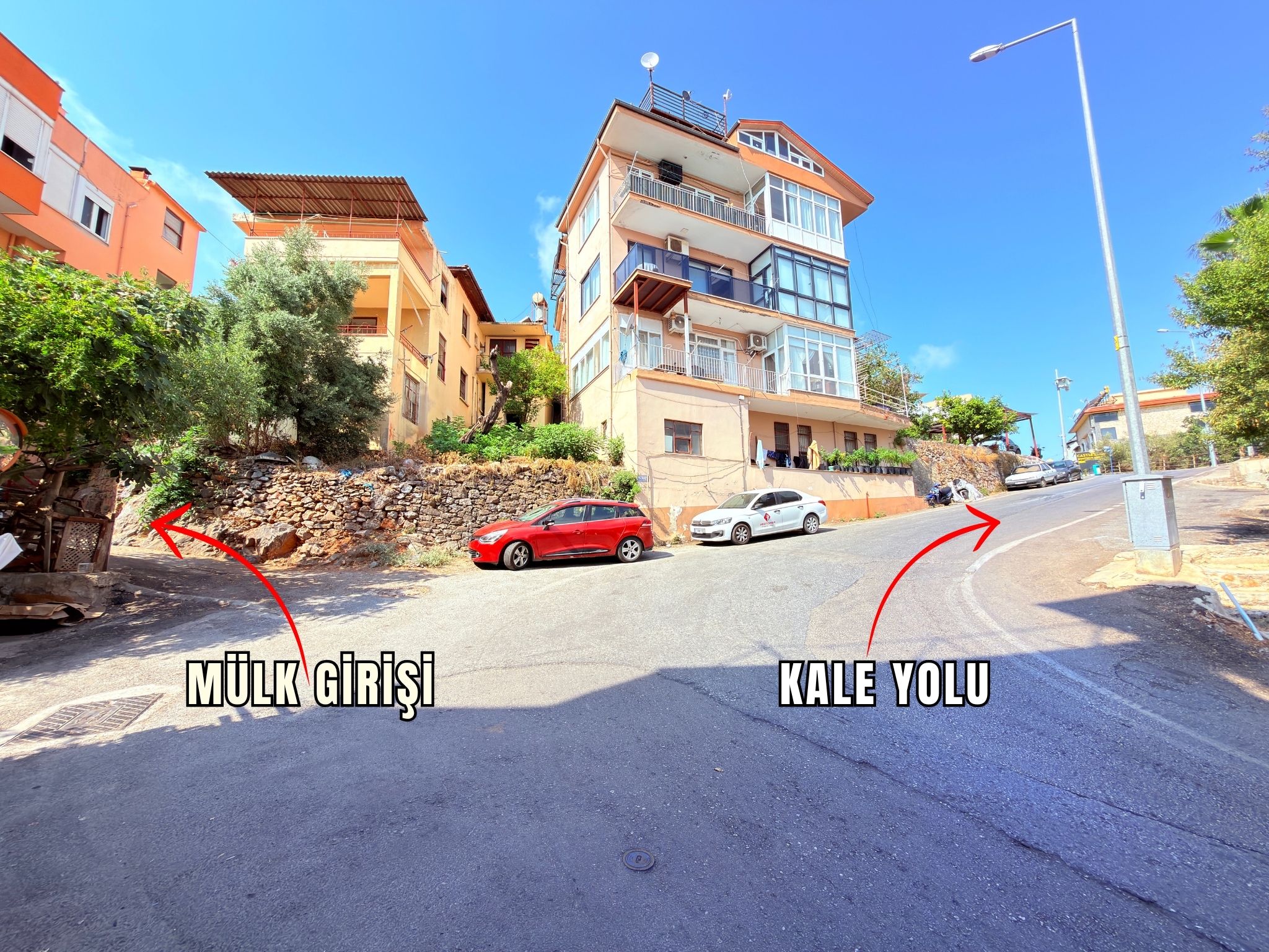 A residential intersection with a retaining wall and olive tree beside a villa in Turkey