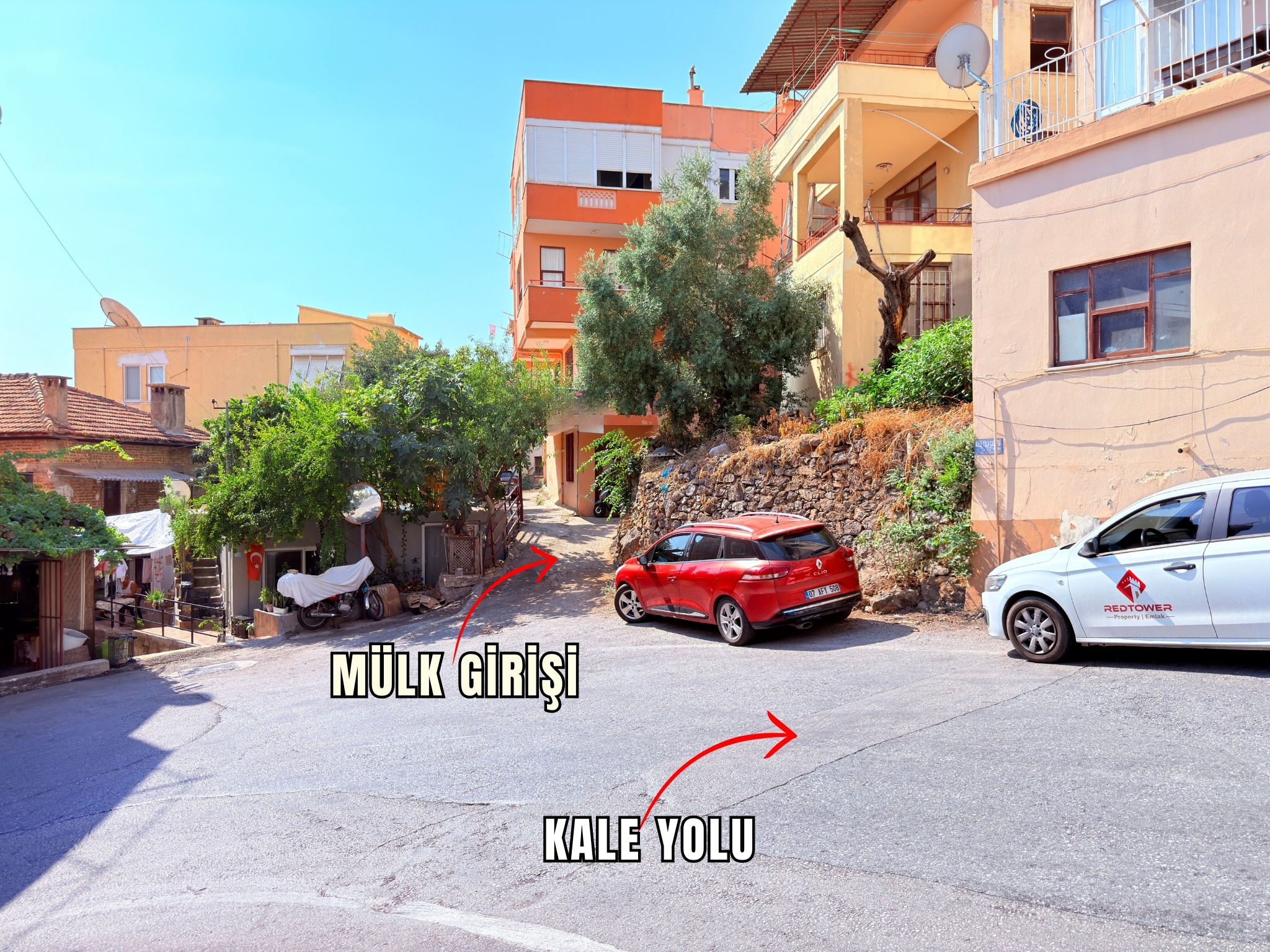 A narrow street with a stone wall, red car and olive tree in Alanya