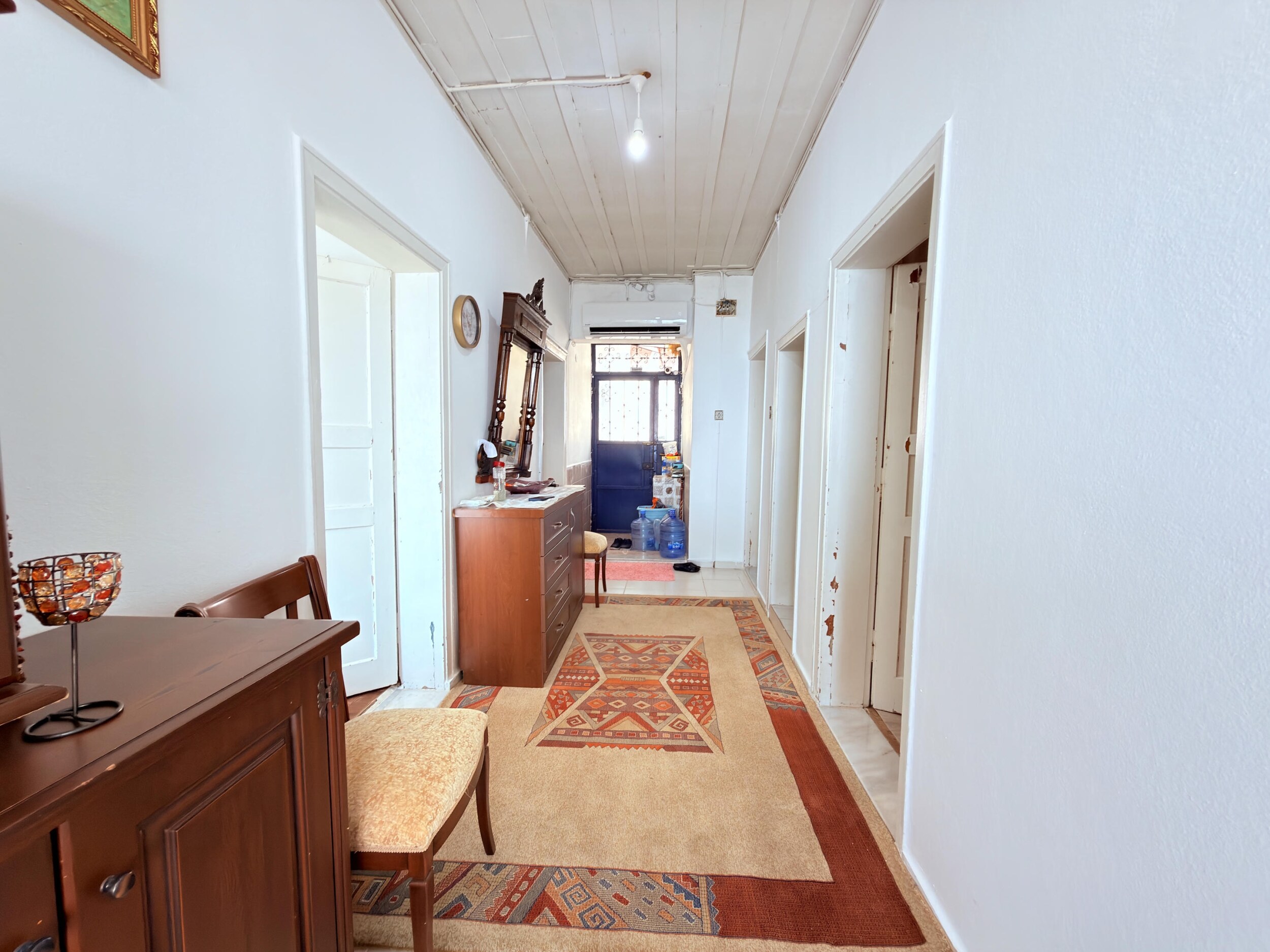 A long white corridor with a wooden chest, patterned runners and several doors