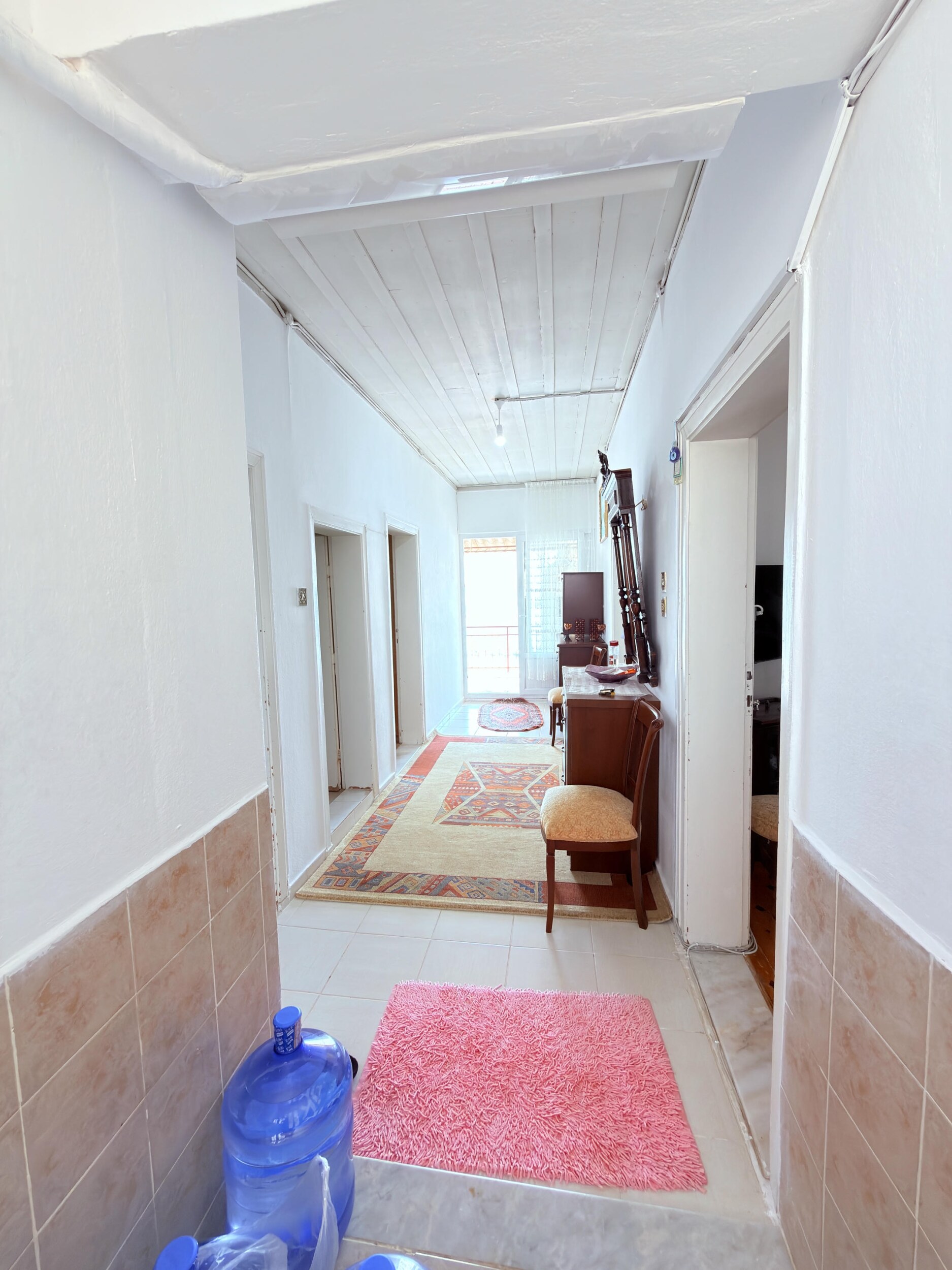 A tiled corridor with a wooden chest, water bottles and several doorways in Alanya
