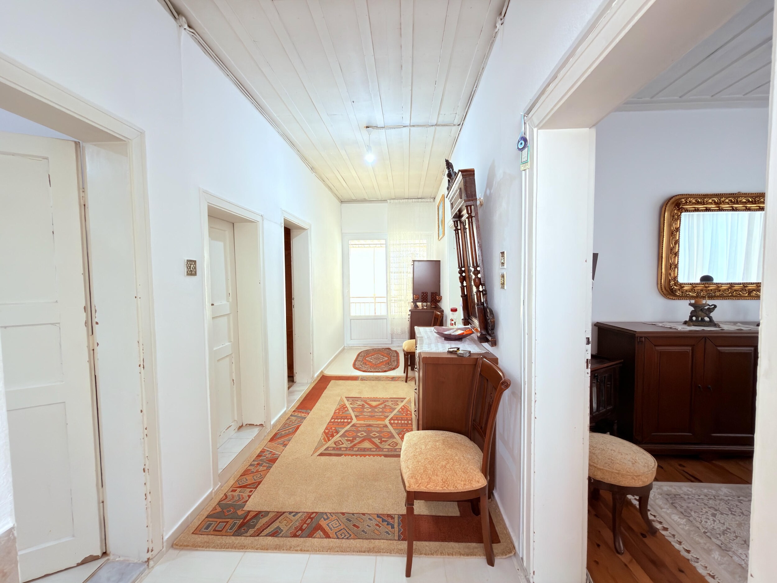 A bright villa corridor with a mirrored chest, patterned runners and several doors