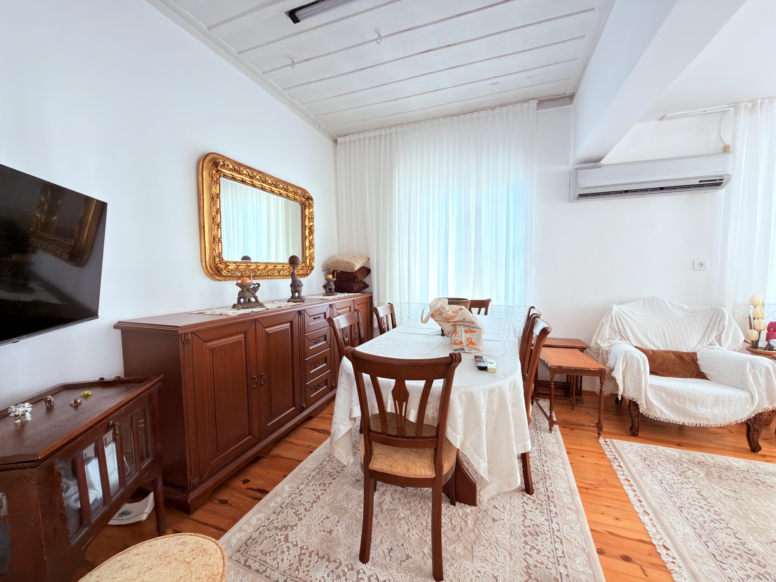 A living room with wooden floors, covered seating and an oval dining table in a villa