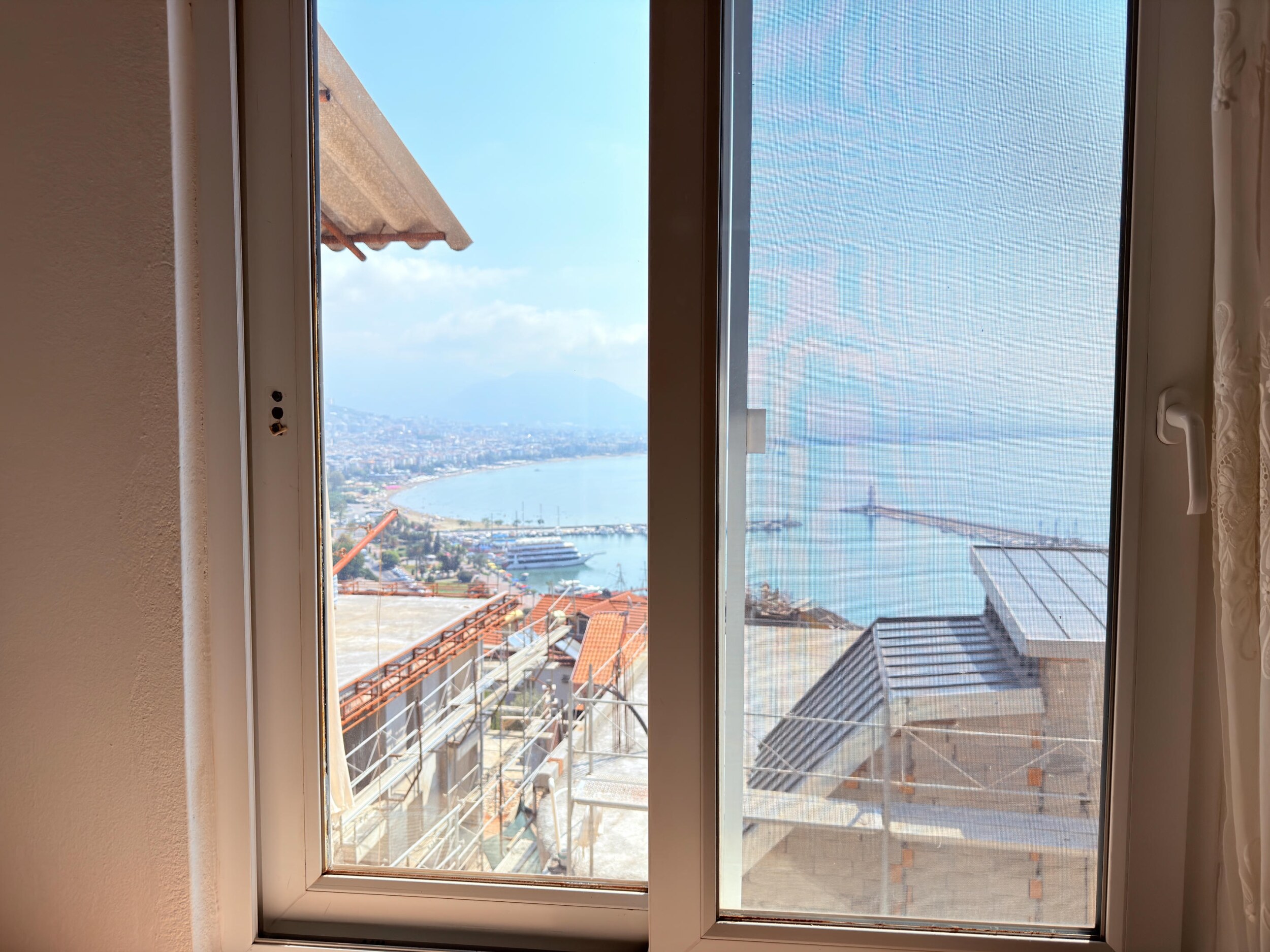A bay view through a double window with port piers and red roofs from a villa
