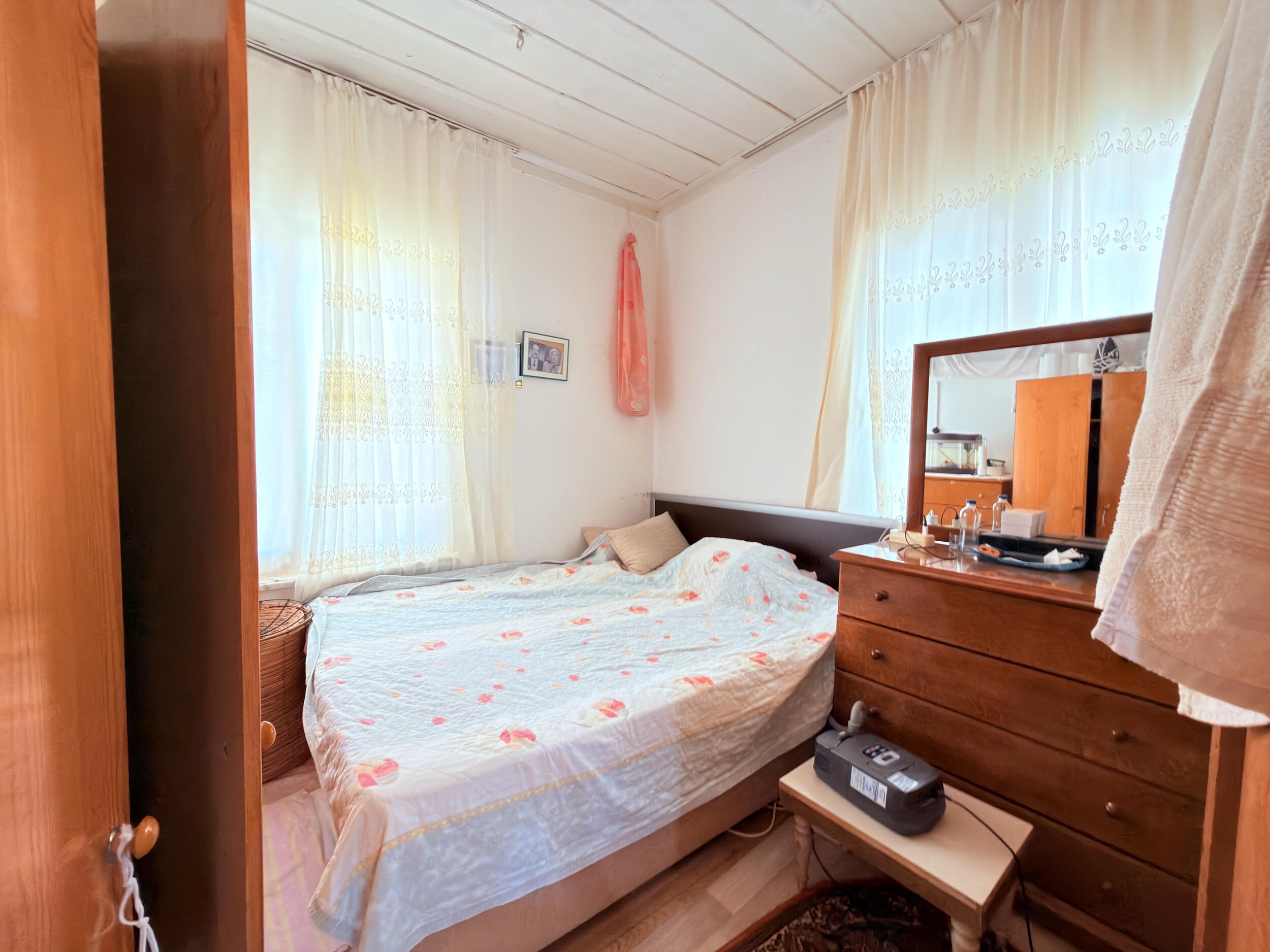 A bedroom with floral bedding, dresser, wardrobe and two windows in a villa in Alanya