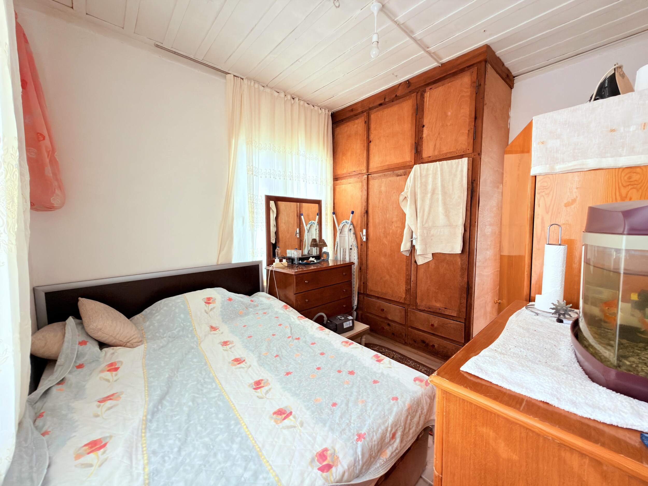 A bedroom with floral bedding, large wooden wardrobe and aquarium