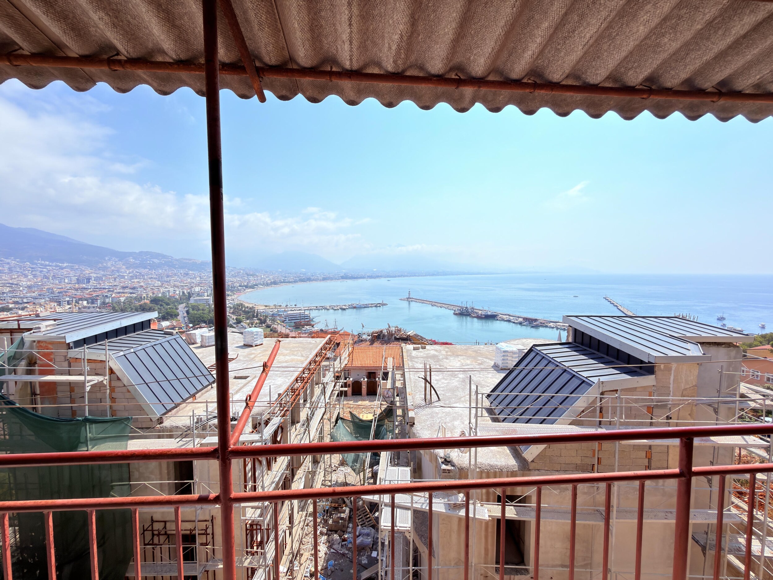 A covered villa terrace with red railings and panoramic bay view