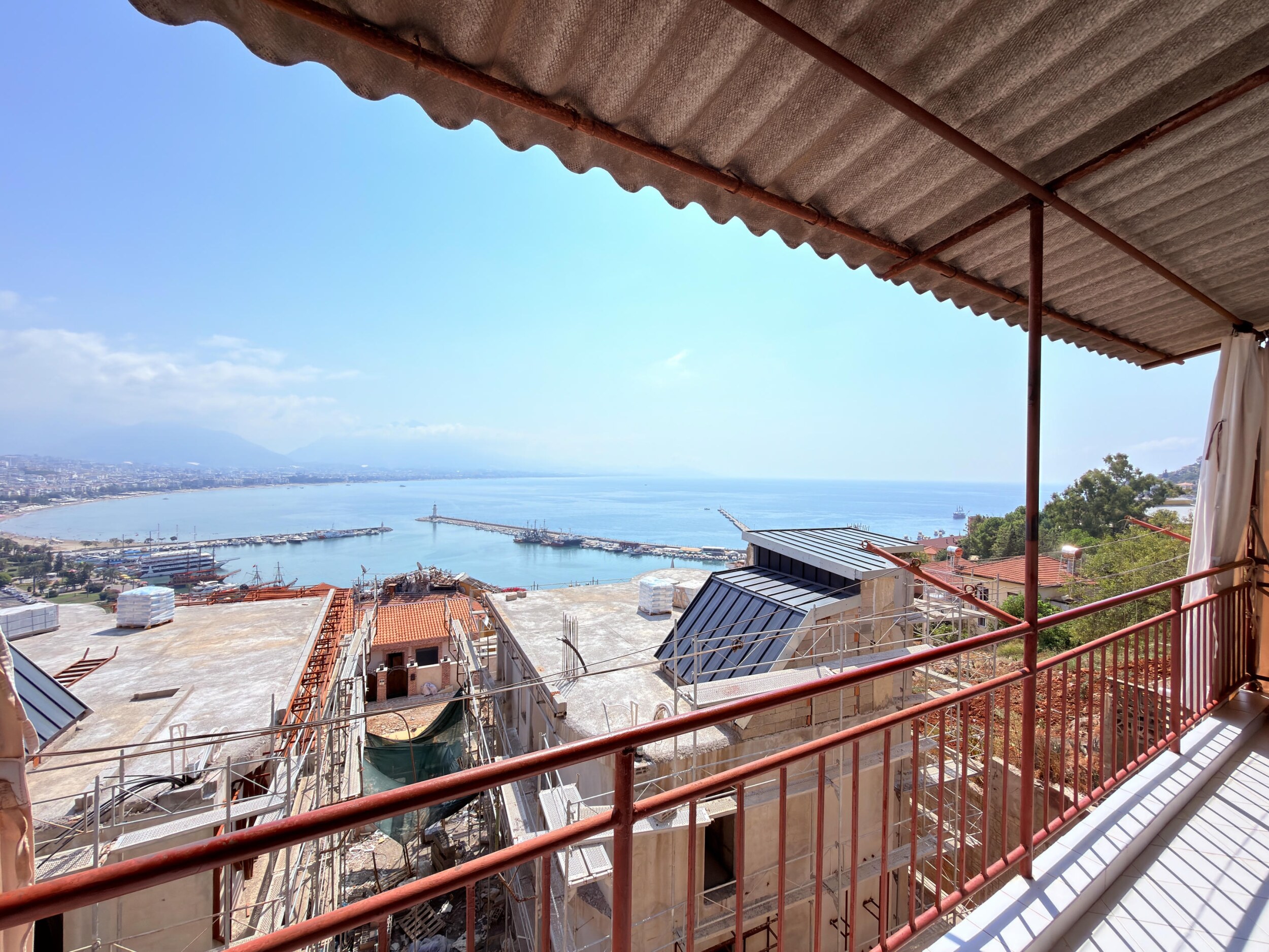 A covered terrace with red railings overlooks a harbor bay and breakwaters at a villa for sale in Alanya