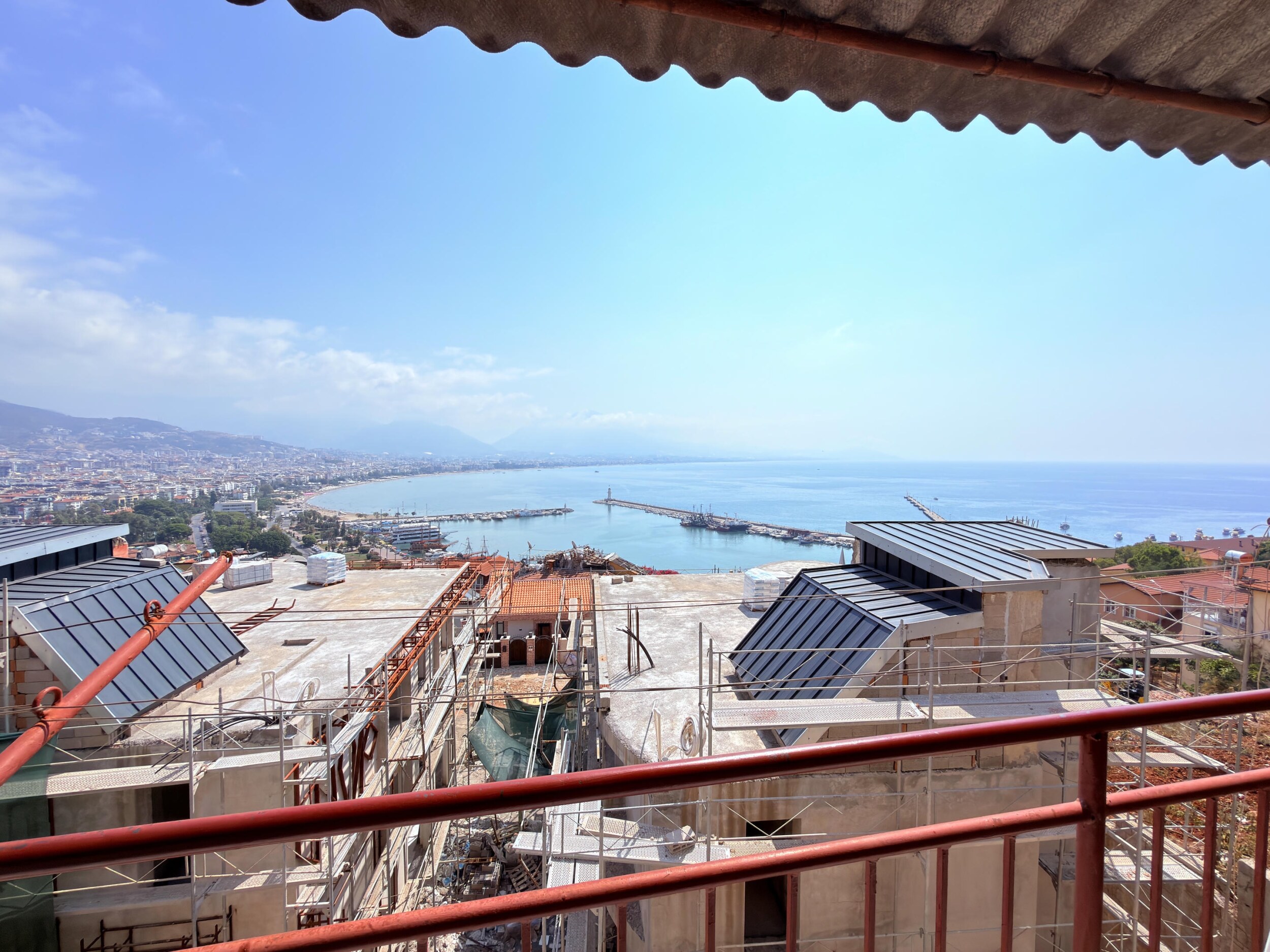 A covered terrace with red railings, harbor breakwaters and bay view belongs to a villa
